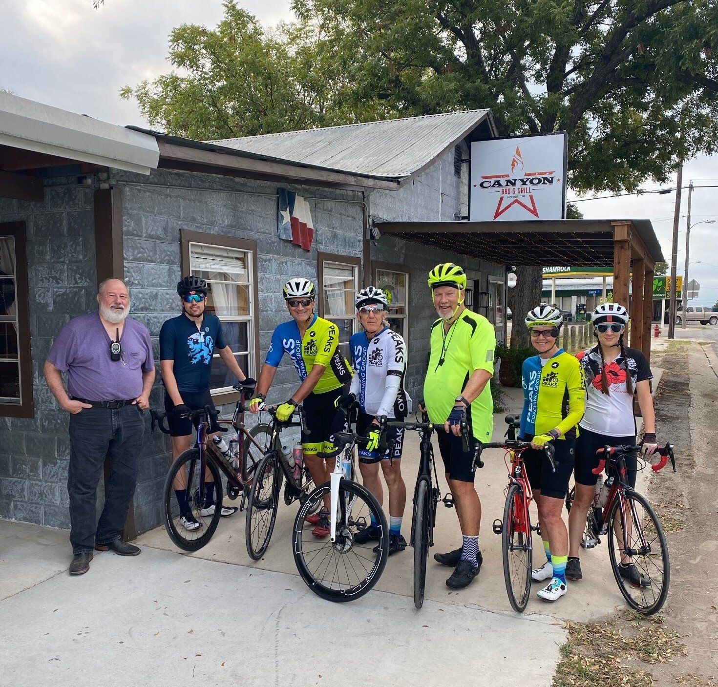 A group of cyclists are posing for a picture in front of a building that says canyon
