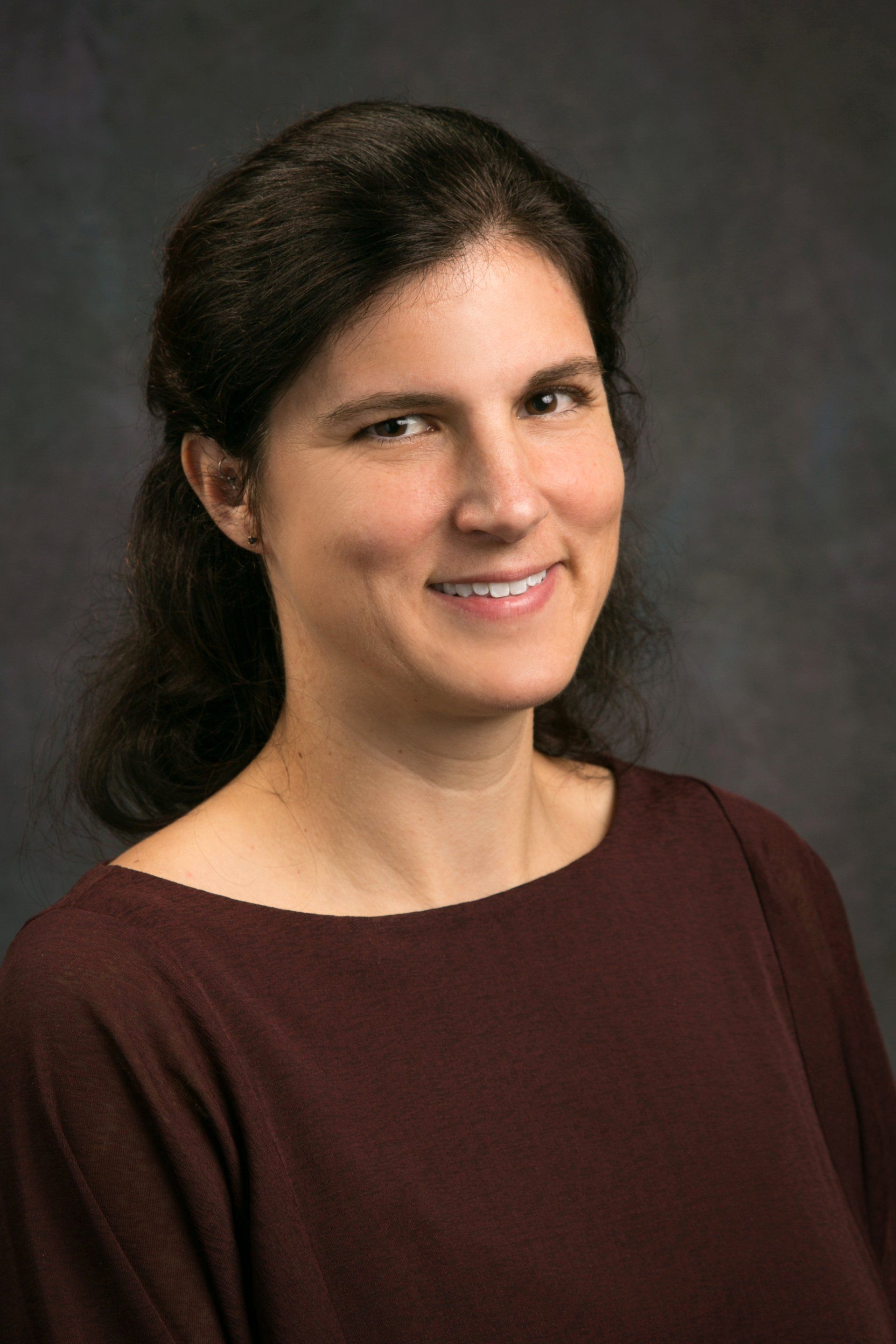 A woman in a maroon shirt is smiling for the camera.