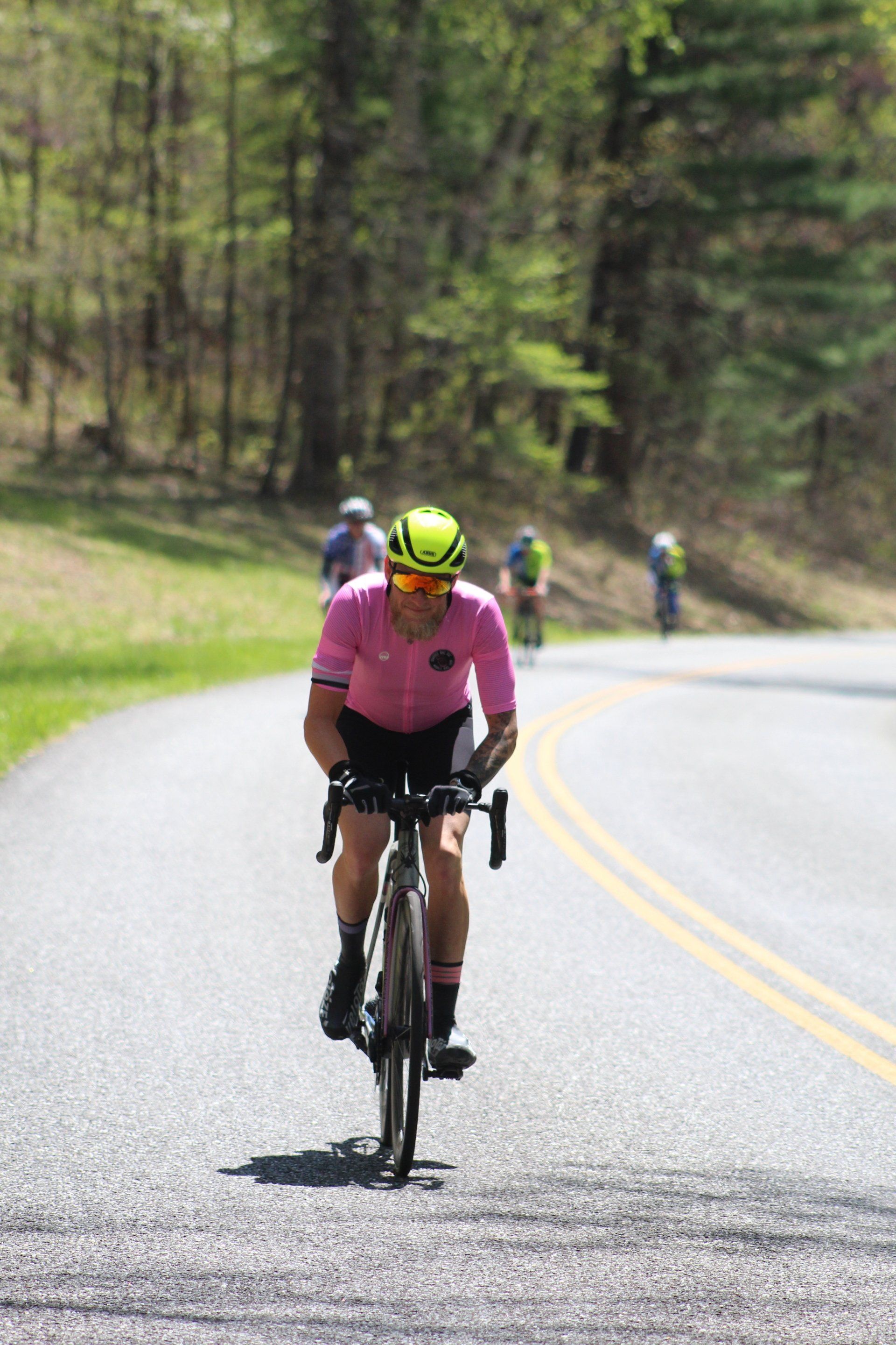A man in a pink shirt is riding a bike down a road.