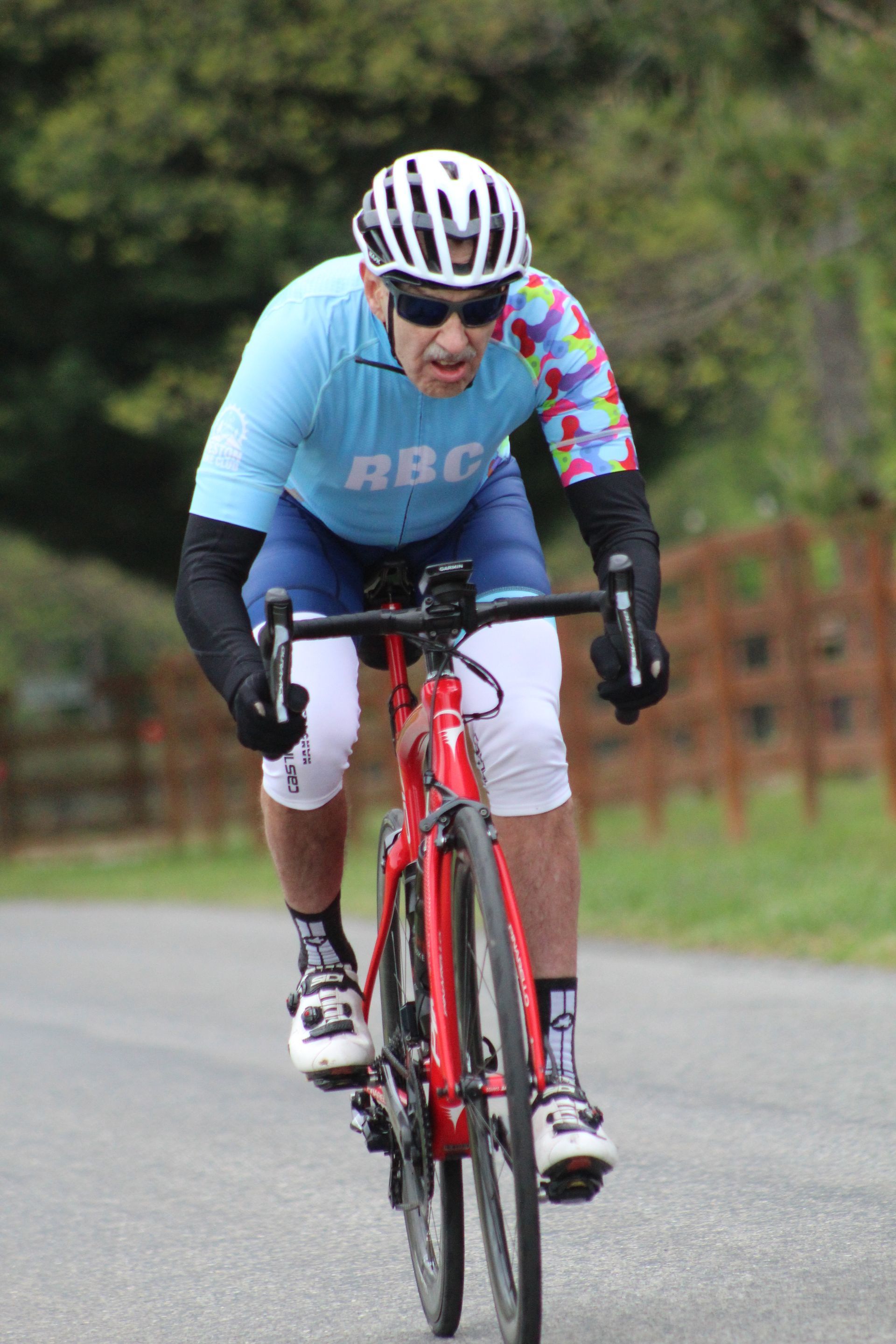A man wearing a helmet and sunglasses is riding a bicycle down a road.
