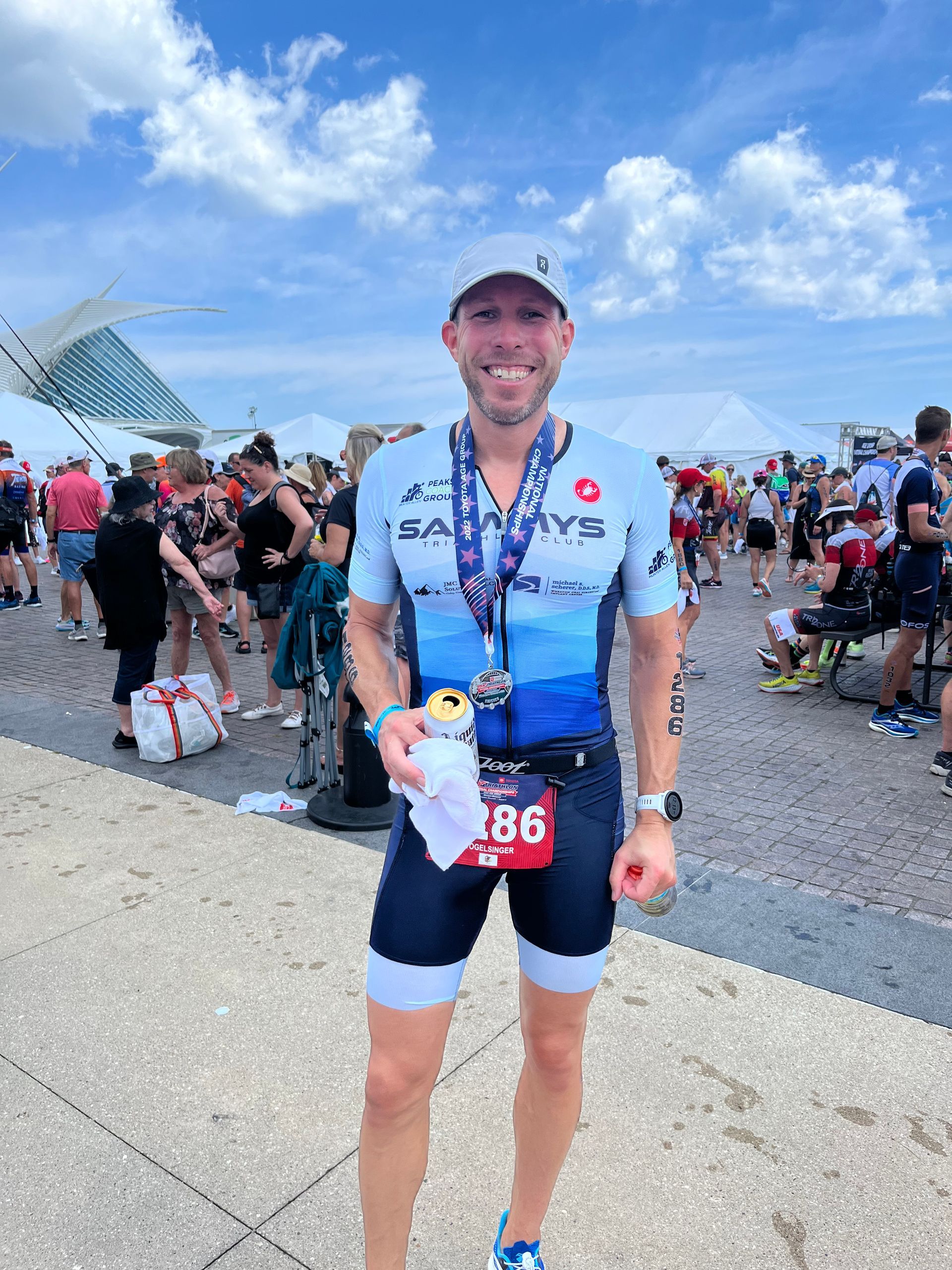 A man in a triathlon outfit is holding a can of soda and a medal.