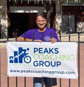 A man in a purple shirt is holding a peaks coaching group banner