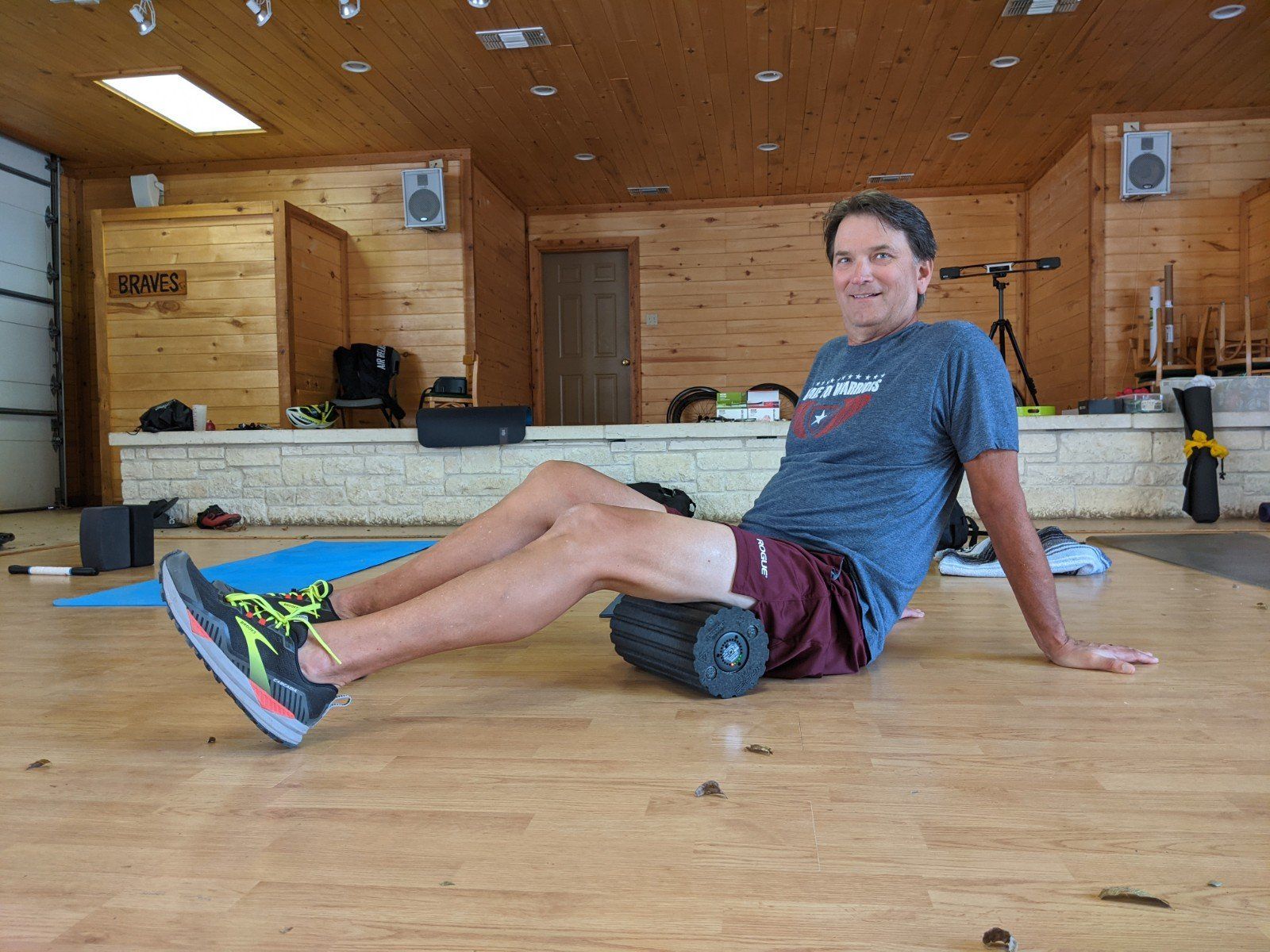 A man is sitting on the floor with a foam roller on his leg.