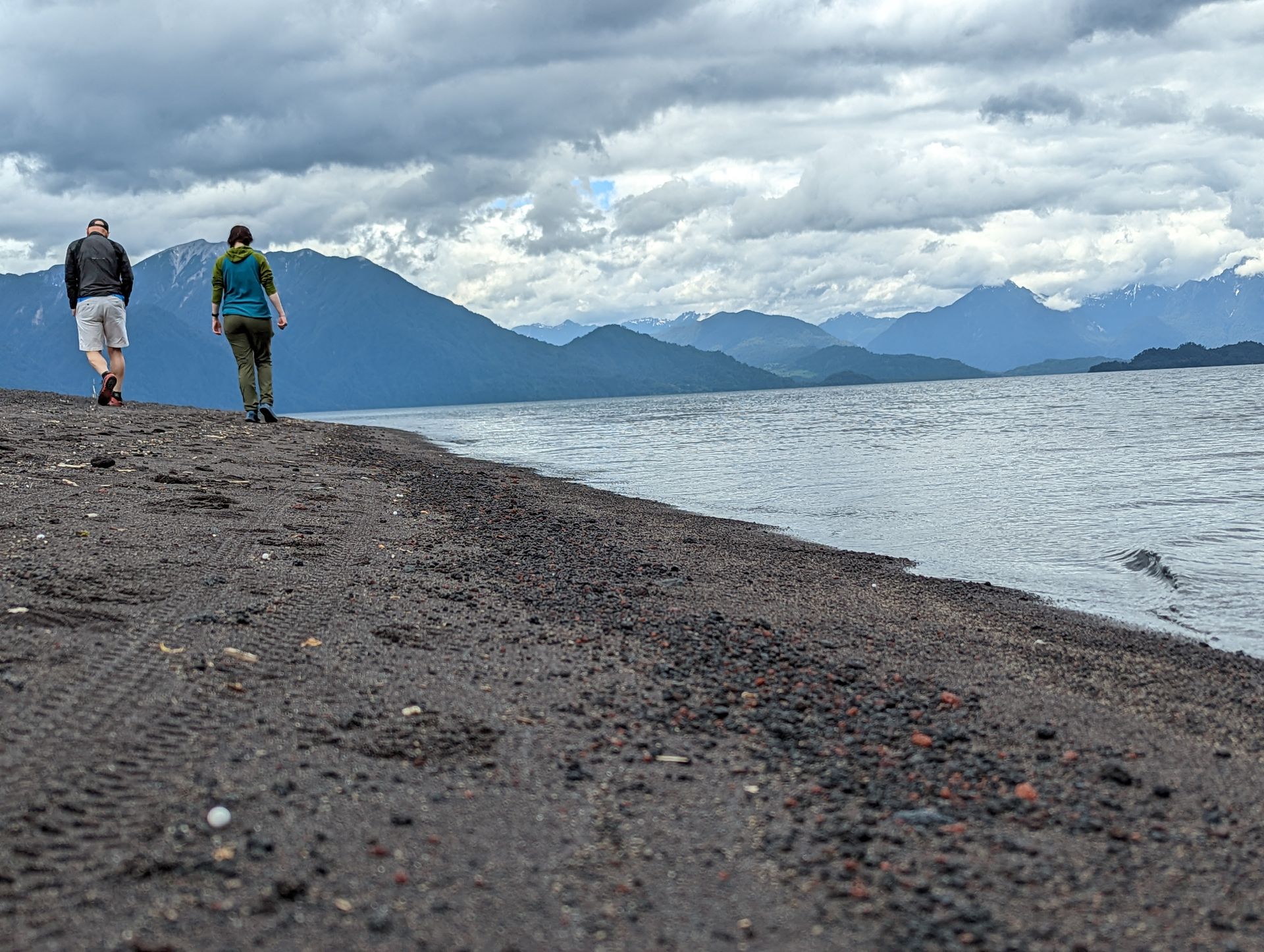 Two people are walking along the shore of a lake.