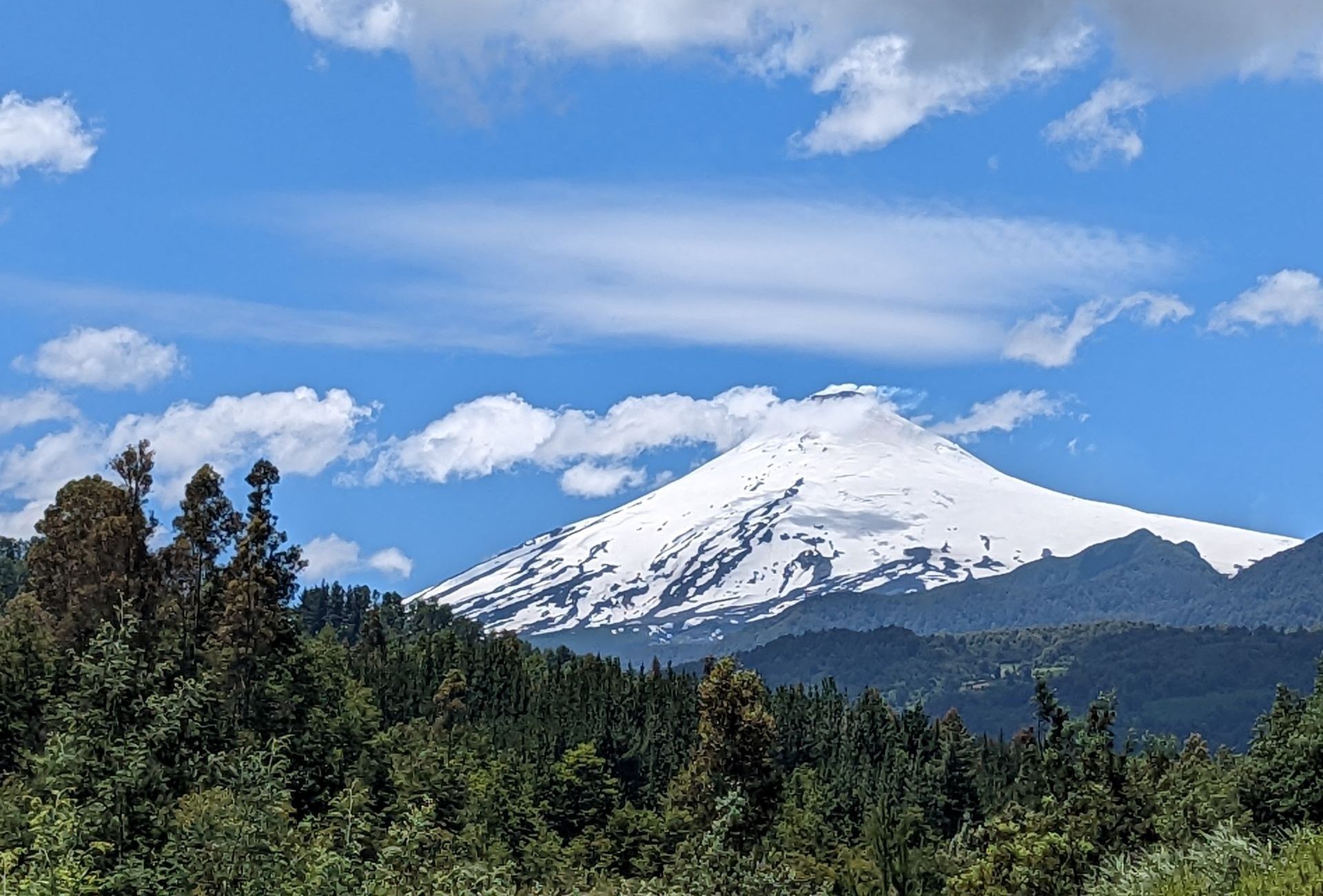 A snowy mountain covered in snow is surrounded by trees on a sunny day.