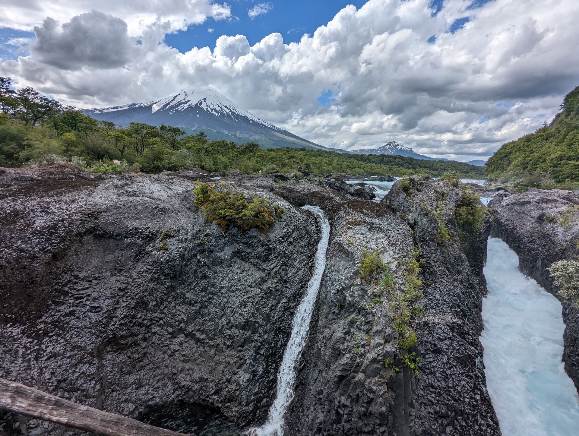 A waterfall in the middle of a canyon with mountains in the background.