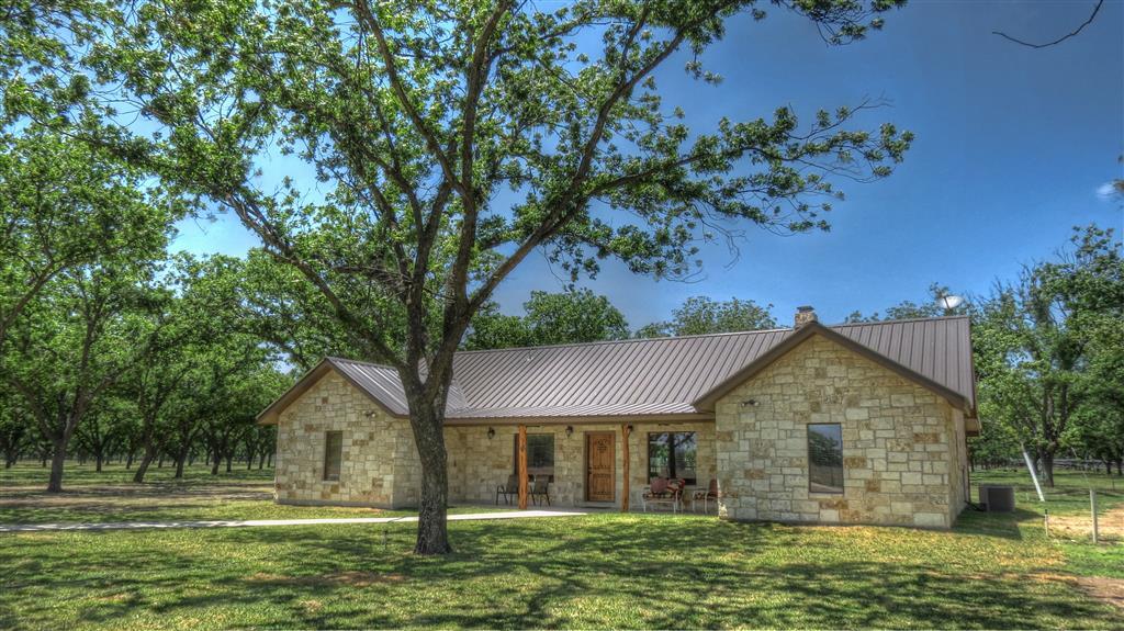 A stone house with a metal roof and a tree in front of it.