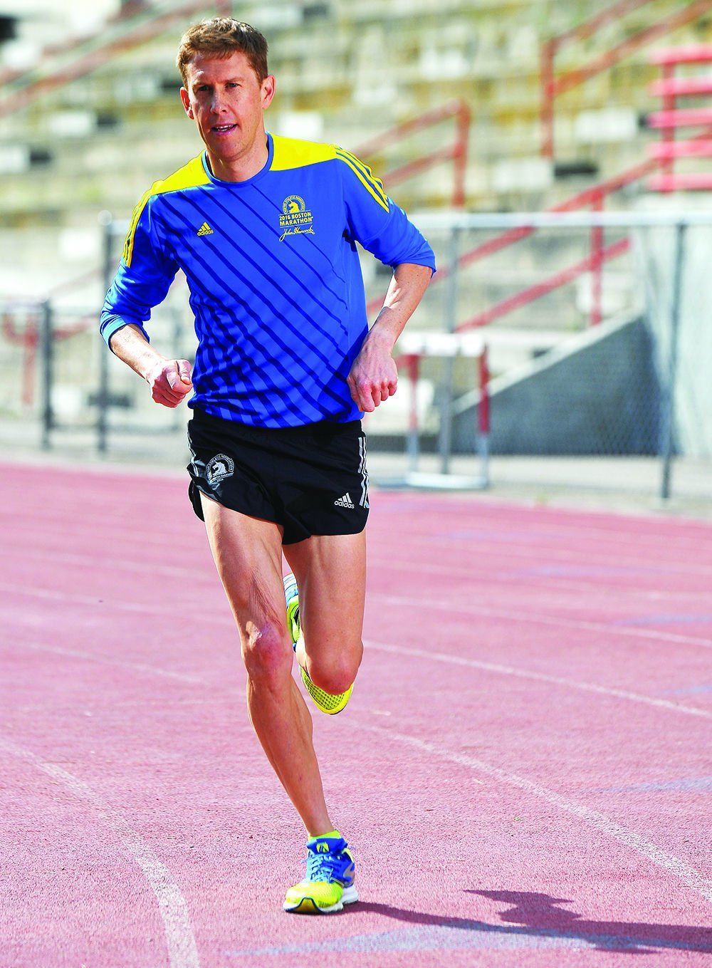 A man in a blue shirt and black shorts is running on a track.