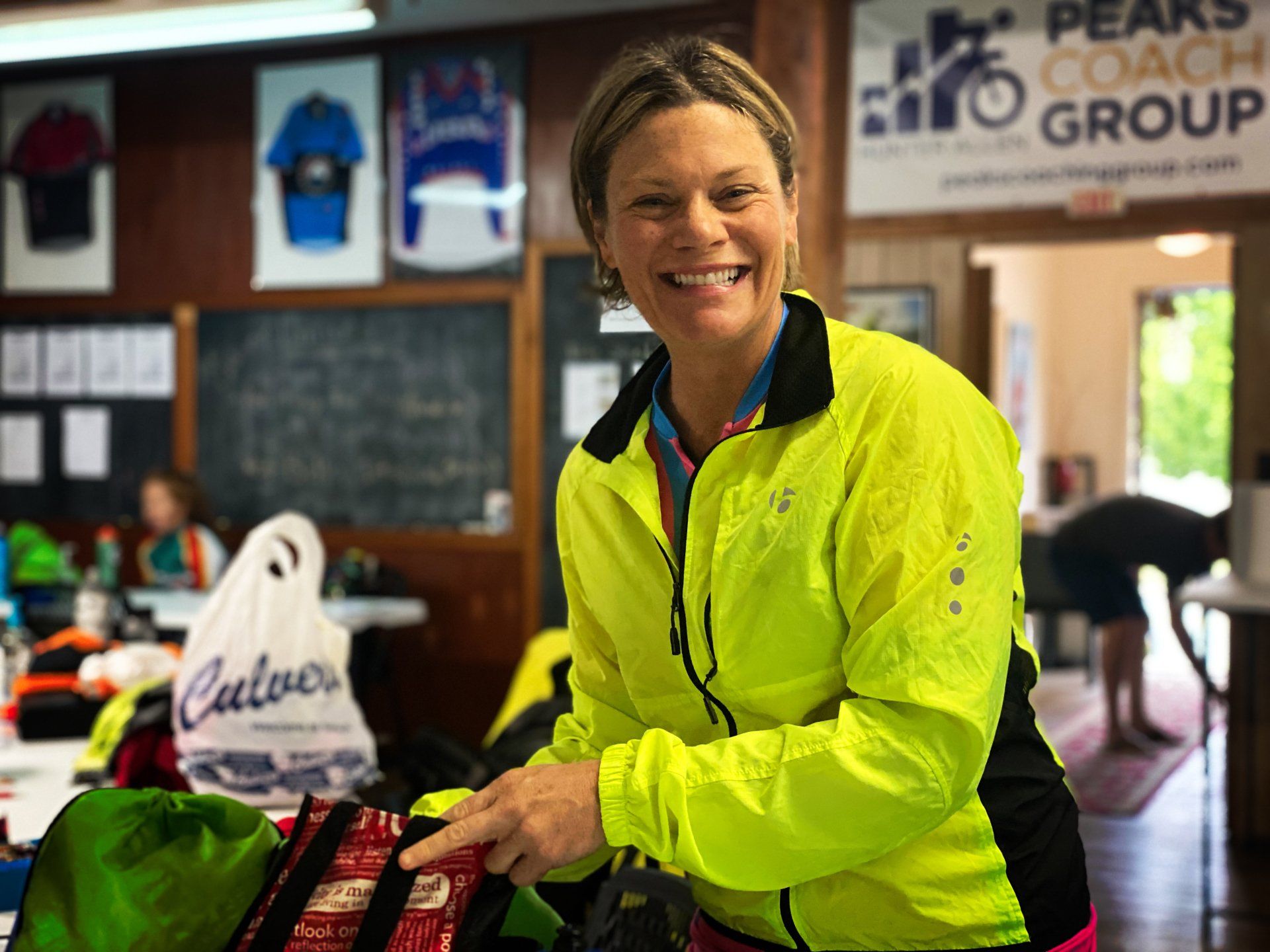 A woman in a yellow jacket is smiling while holding a green bag.