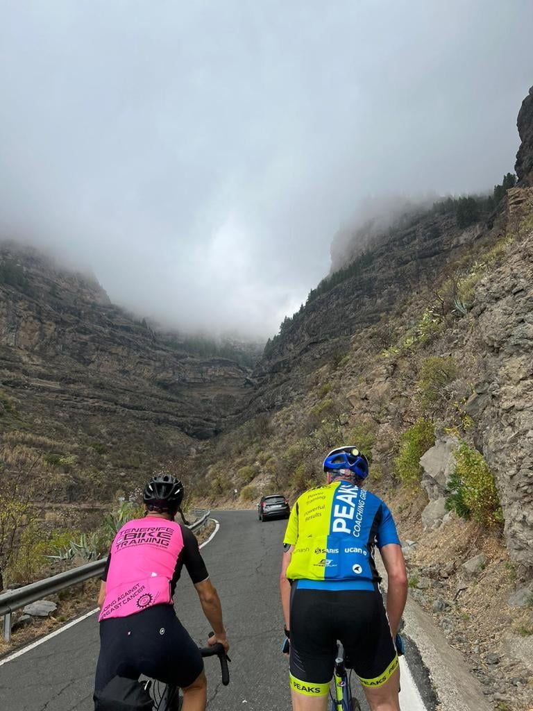 Two people are riding bicycles down a mountain road.