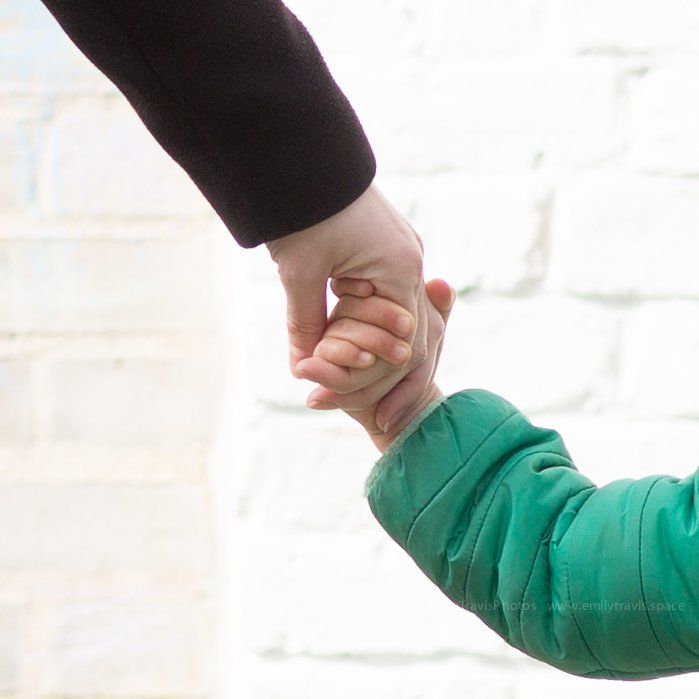 Adult and child holding hands against a white brick background