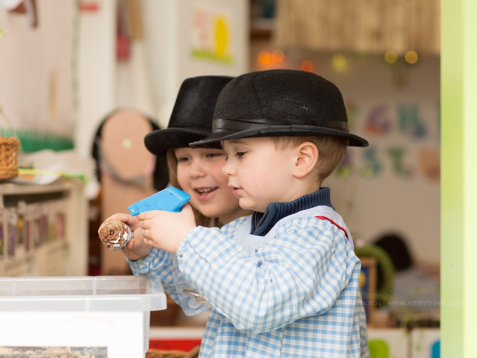 Two children in black hats playing with a toy at a table in a classroom