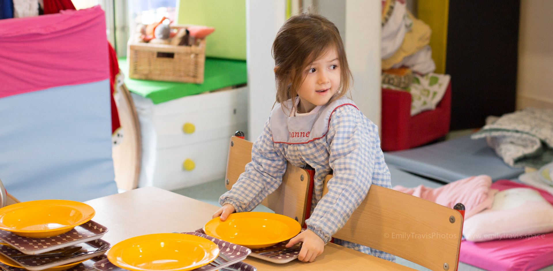 Toddler kneeling at a table with orange plates in a colorful playroom