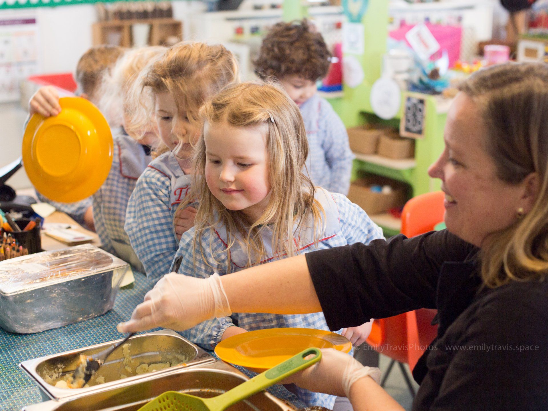 Children serving food at a buffet table with an adult assisting them