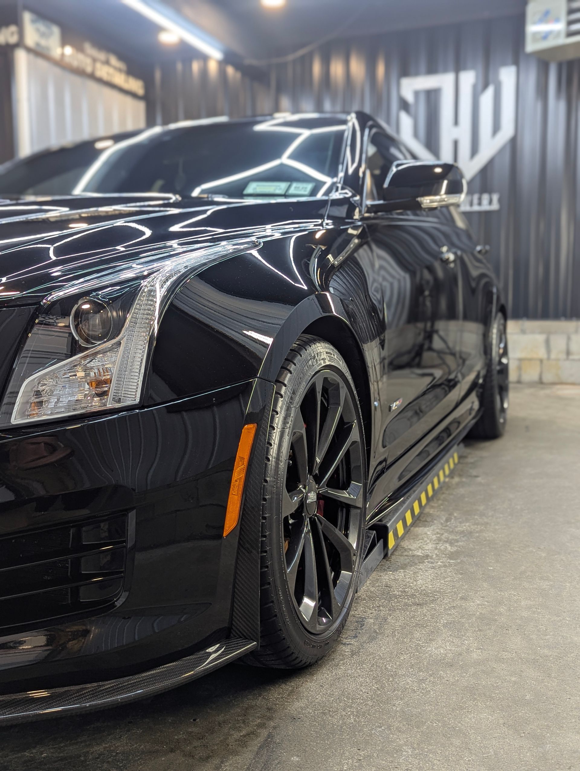 Black Cadillac ATS coupe, glossy and clean, parked in a car wash bay with the side view visible.