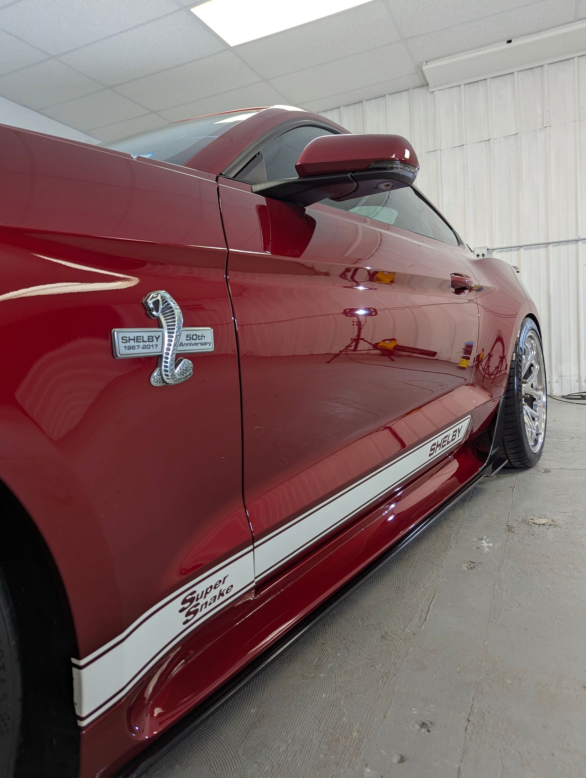 Red Ford Shelby GT350 with white racing stripes; parked indoors.