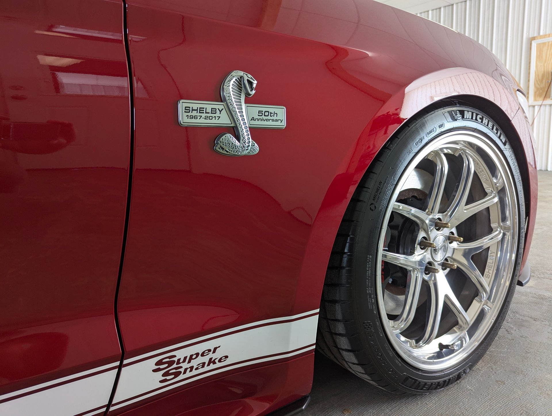 Red Shelby Super Snake car with chrome wheels and snake emblem.