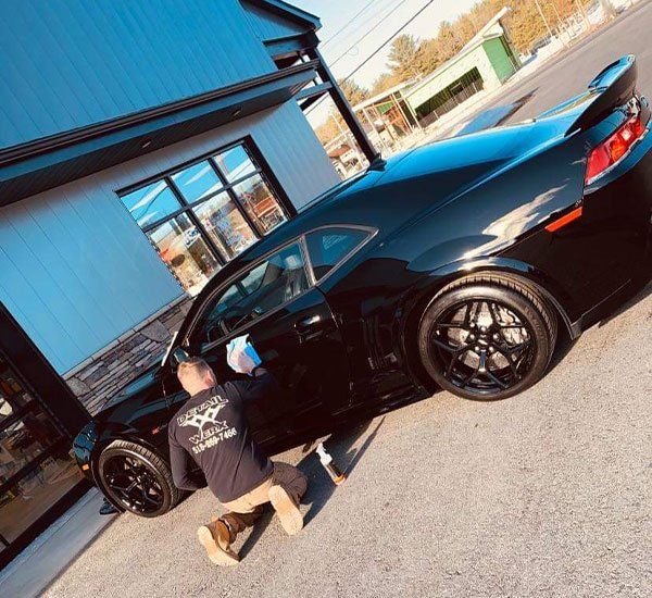 A man is kneeling down next to a black car