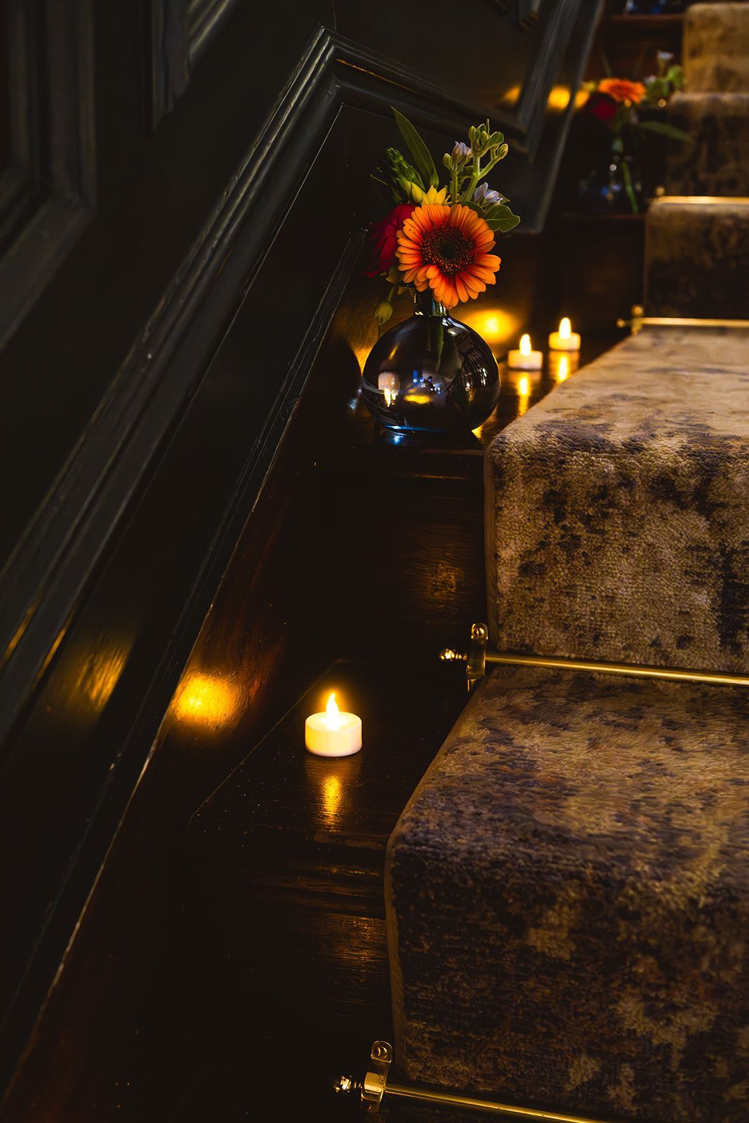 Dim candlelit staircase with a black vase of orange flowers and stone steps