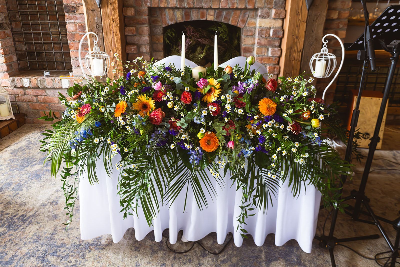 Colorful flower arrangement in white planters beside a brick fireplace and staircase