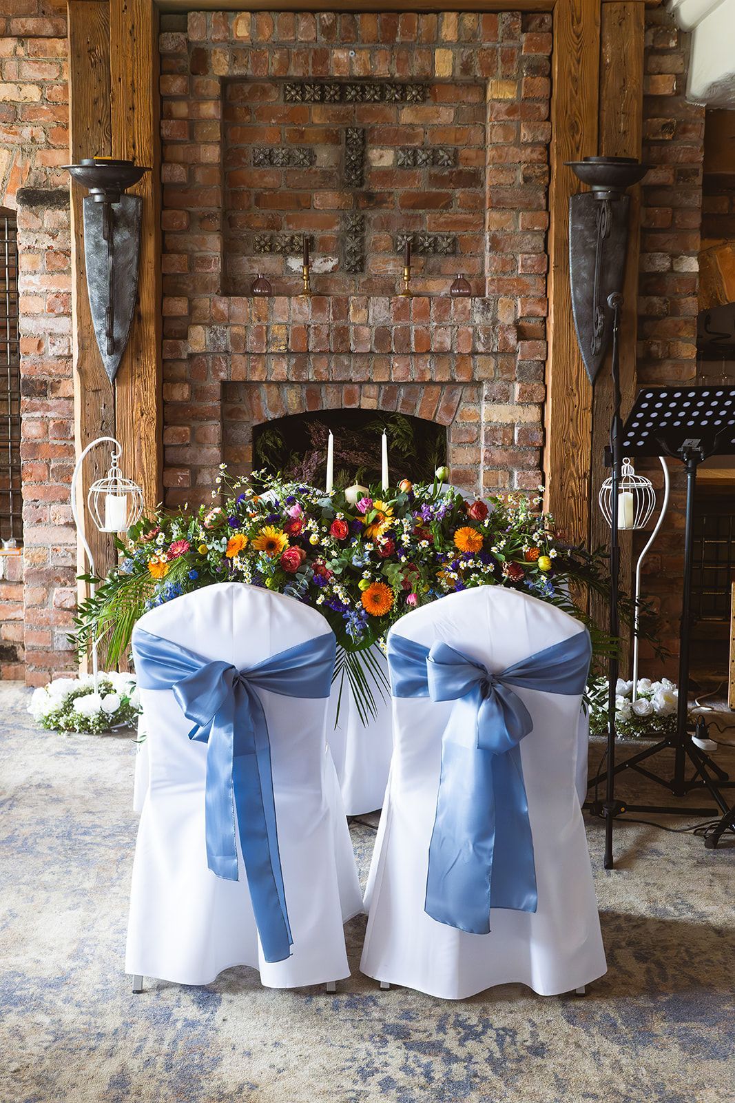 Two white chairs with blue bows before a floral altar backdrop and brick fireplace