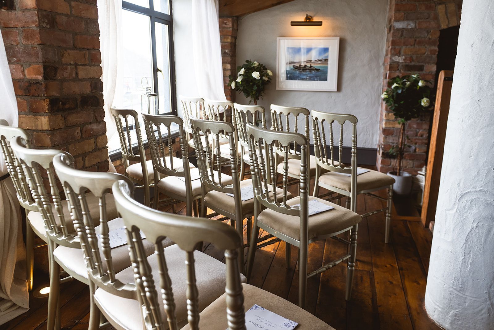 Empty rustic dining room with wooden chairs around a table, brick walls, and a window with white curtains