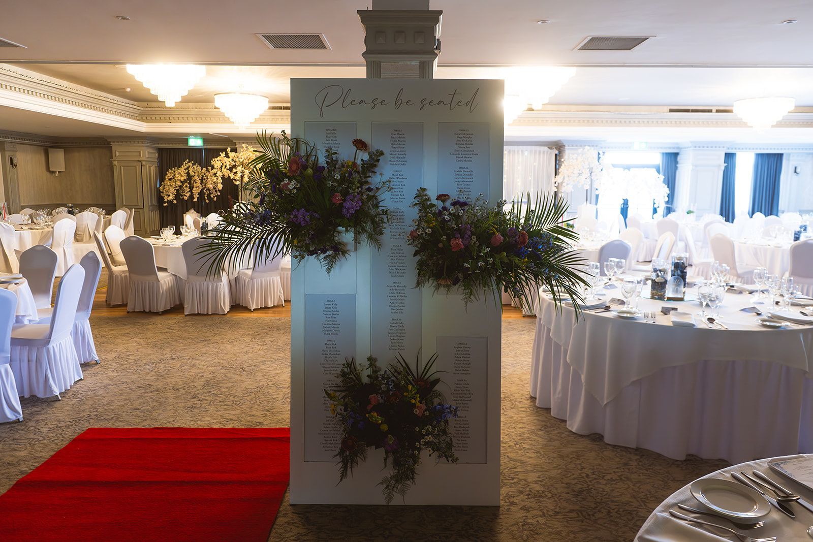 Banquet hall with round tables, white chair covers, floral arrangements, and a red carpet aisle