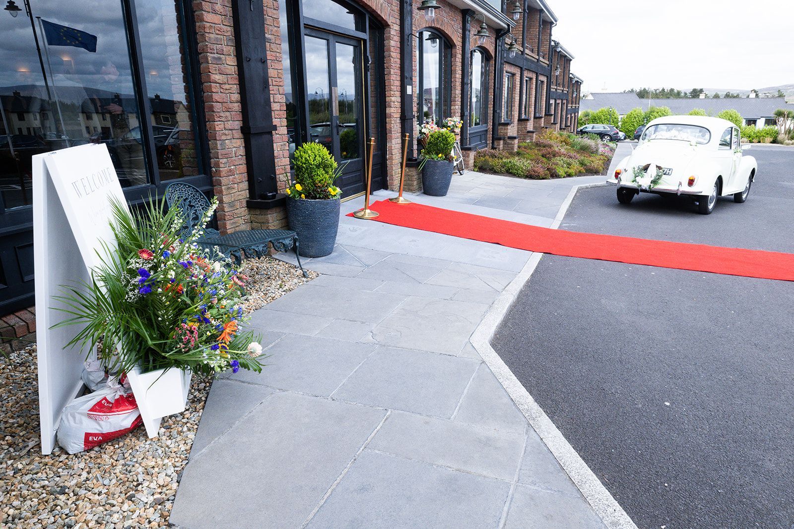 Red carpet outside brick building with white vintage car and flower pots by the entrance