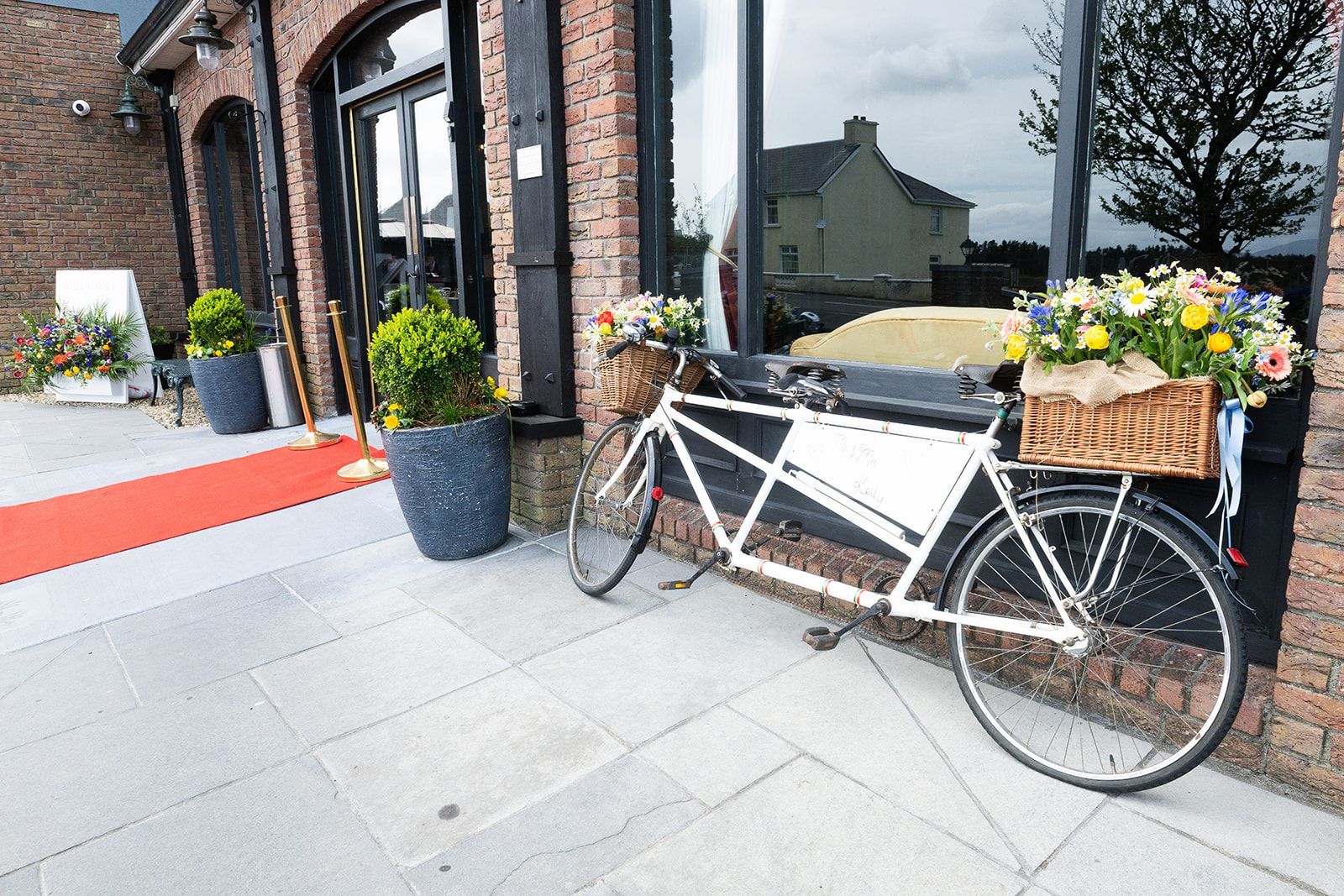 Bicycle parked outside a storefront with potted flowers and a red carpet entrance