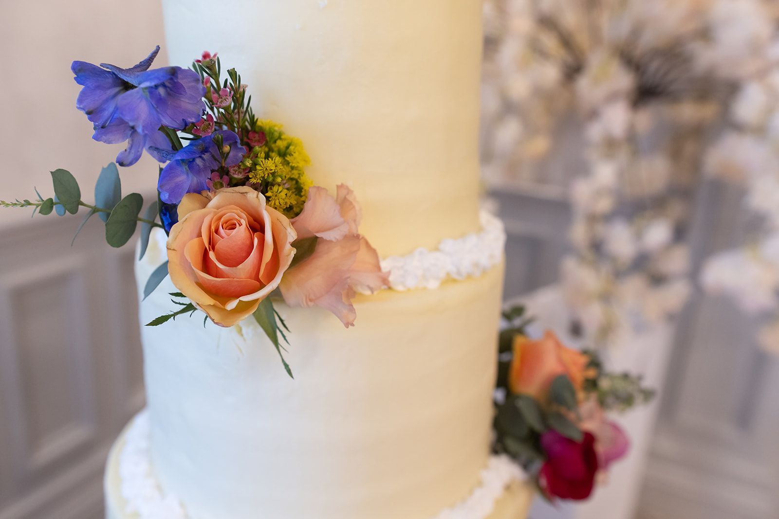 White tiered cake with peach and purple flowers and white ribbon trim