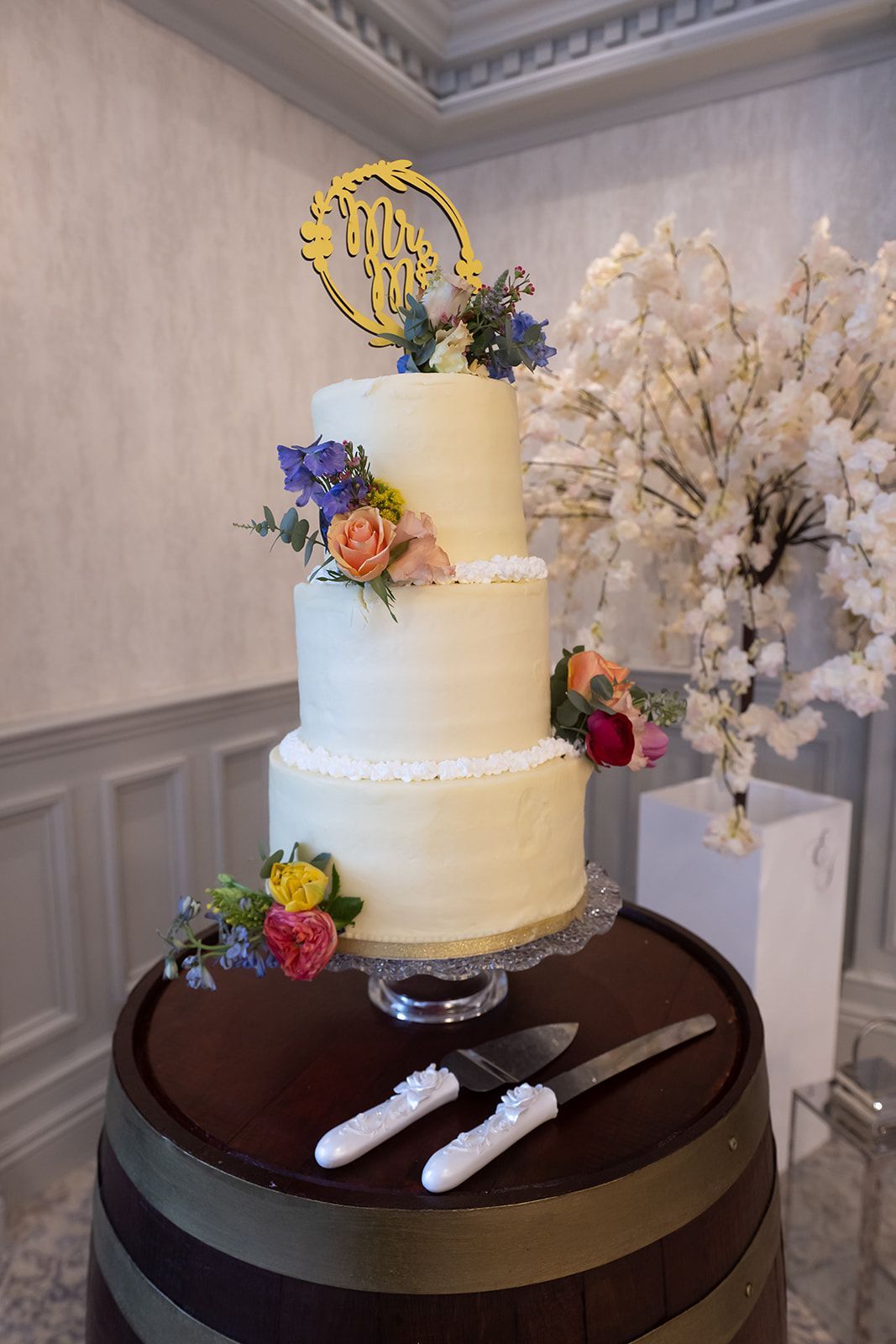 Three-tier white cake with floral accents on a dark dessert table in a decorated room