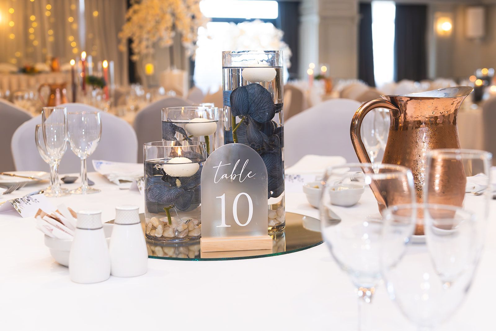 Elegant banquet table set with glassware, candles, and table number 10 in a bright reception hall