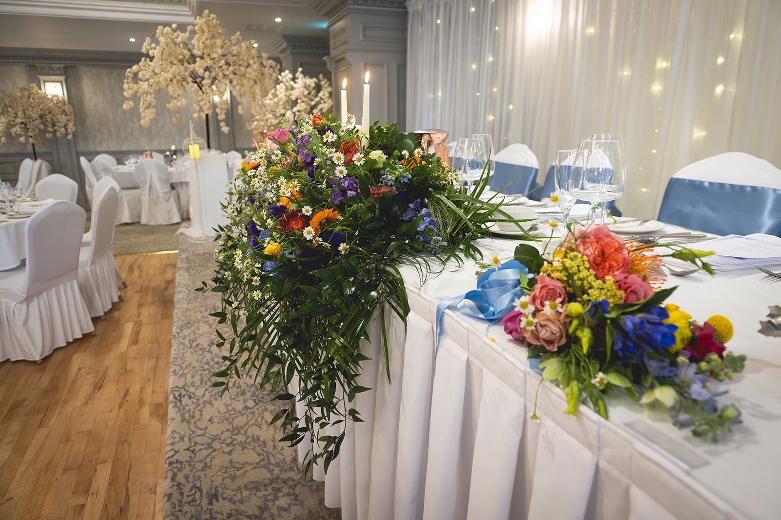 Elegant banquet hall with white chairs, floral centerpieces, and twinkling string lights
