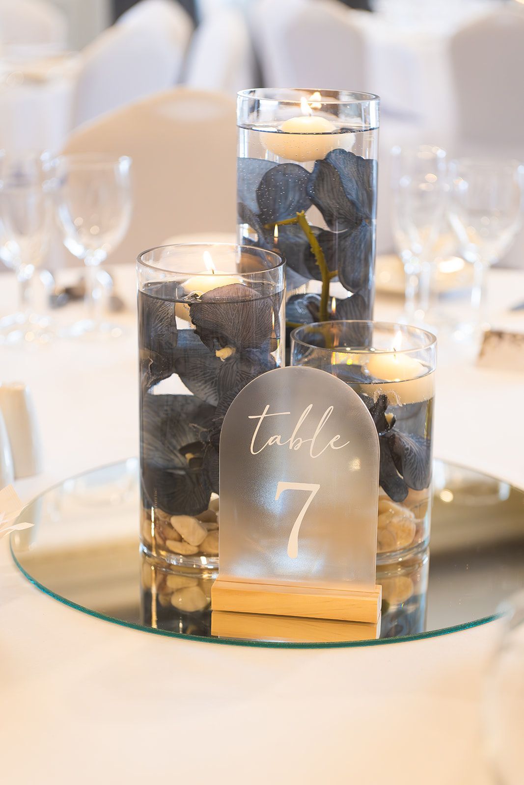 Three glass candle holders with black stones and a gold “table 7” sign on a banquet table