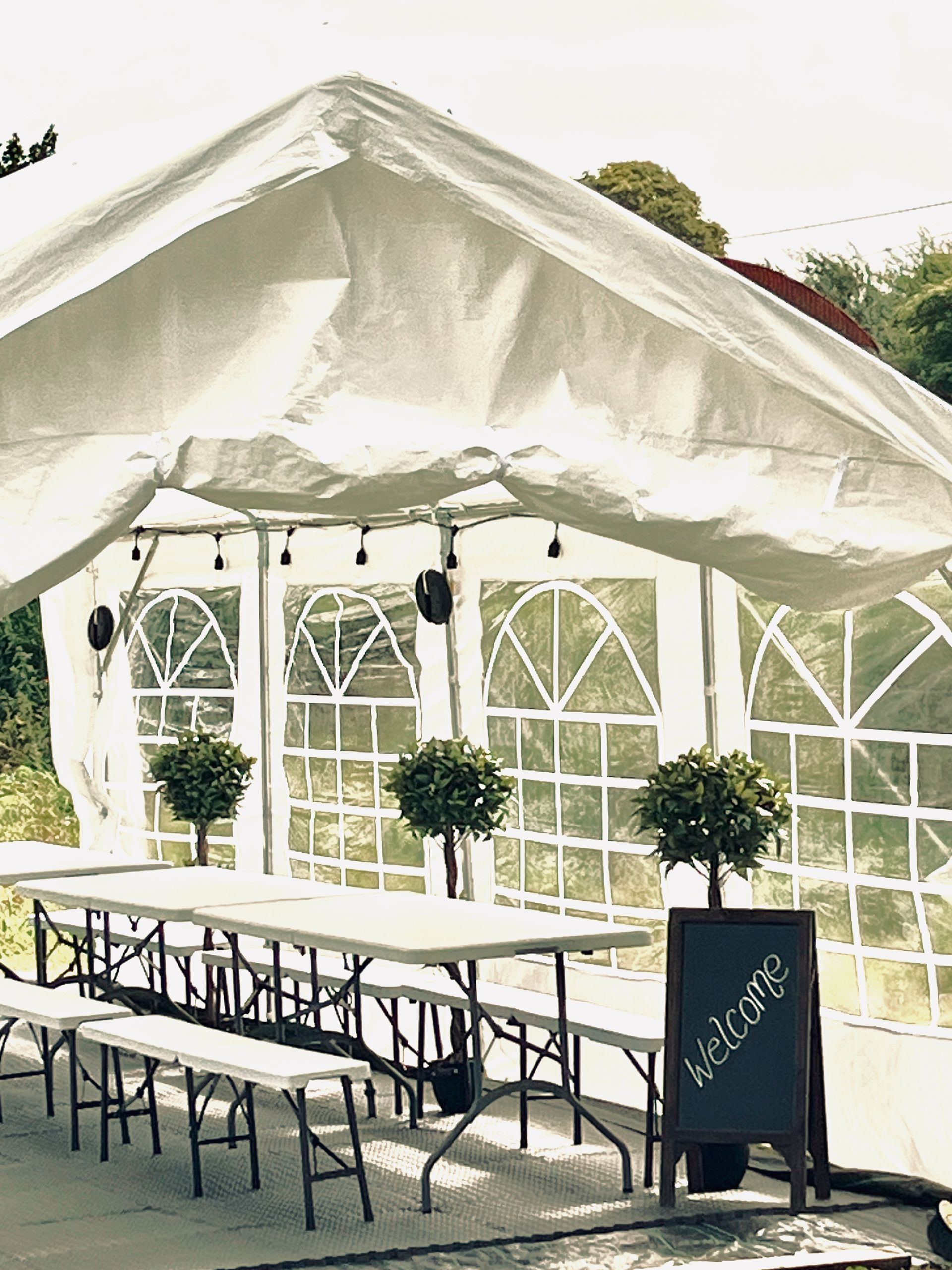 White tented outdoor event space with long tables, benches, and arched window panels