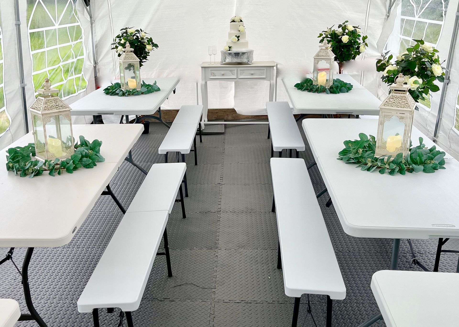White banquet tent with long tables, benches, and floral centerpieces set for an elegant event