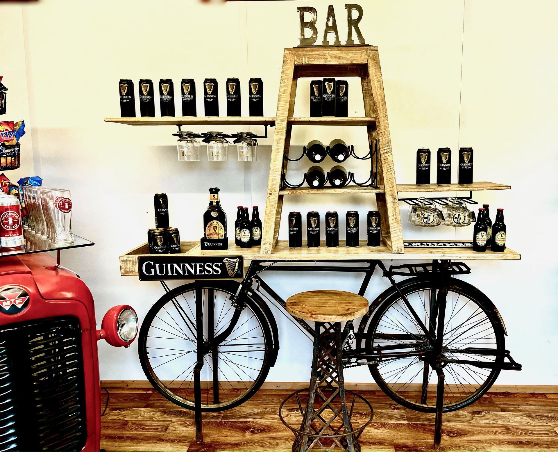 Vintage bicycle bar shelf with Guinness bottles and glasses on a white wall, next to a red jukebox.