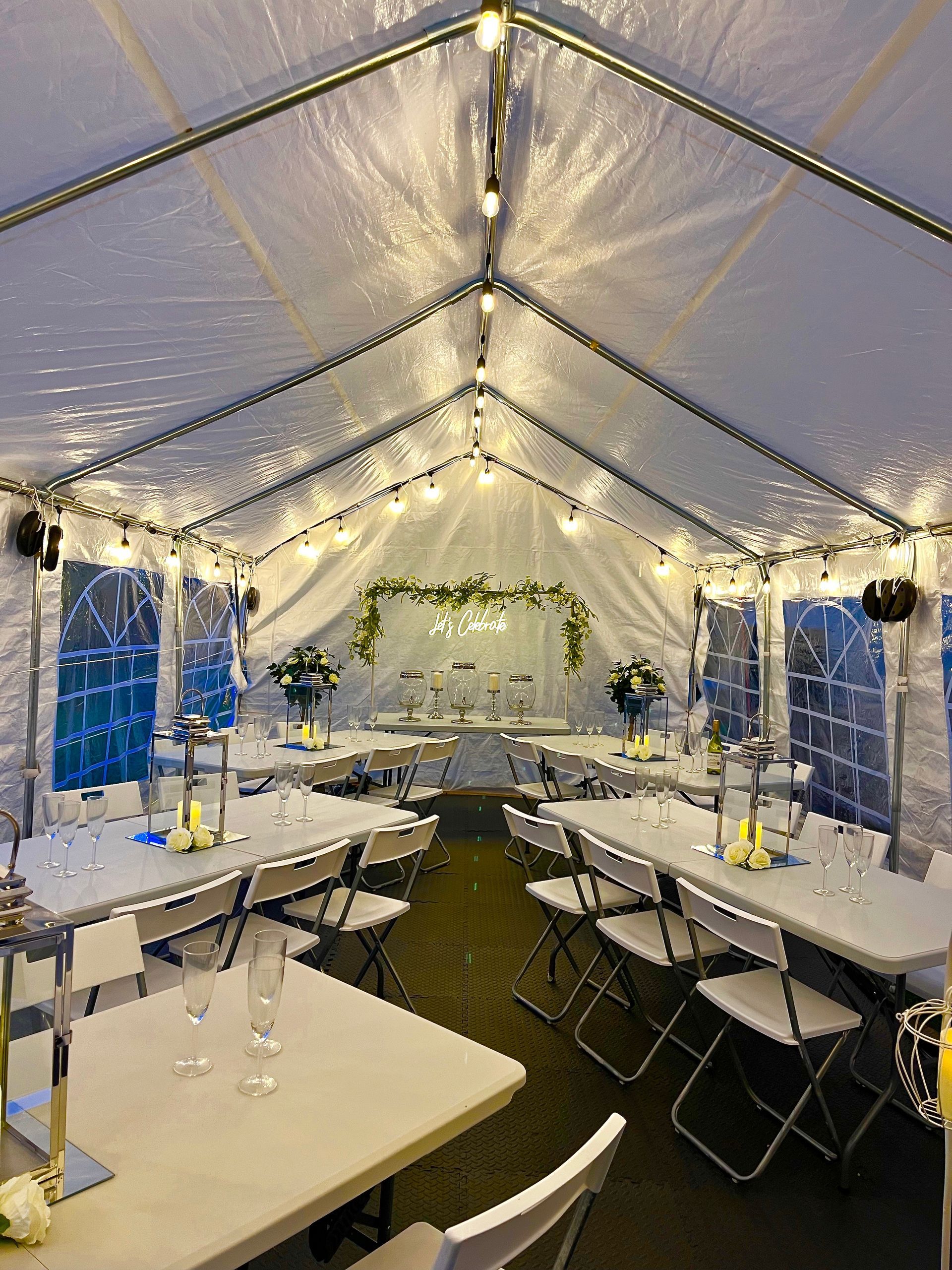 Decorated clear tent with banquet tables, white tablecloths, string lights, and greenery for an event