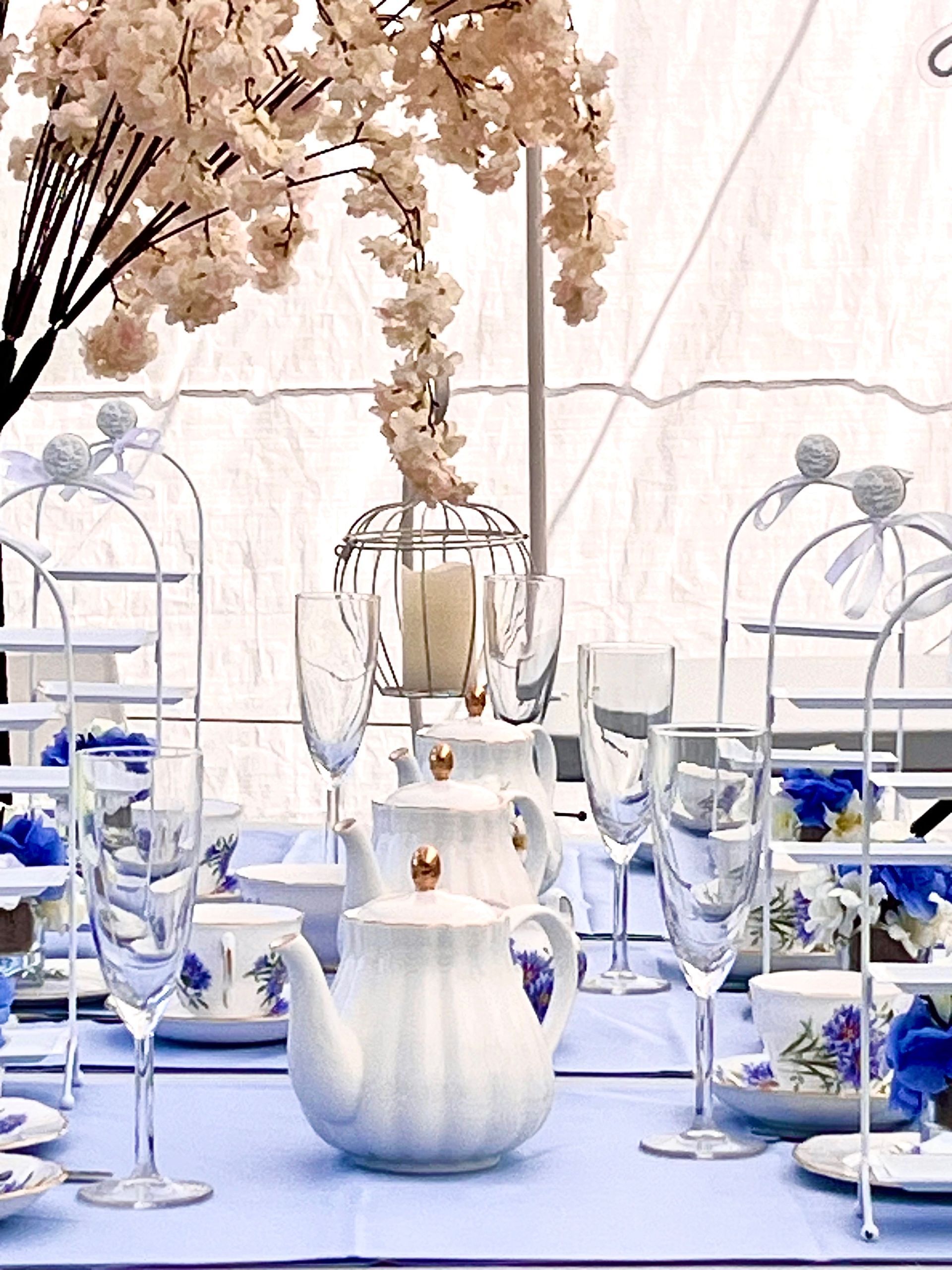 Elegant white tea party table with blue accents, glassware, and floral branches in a bright setting