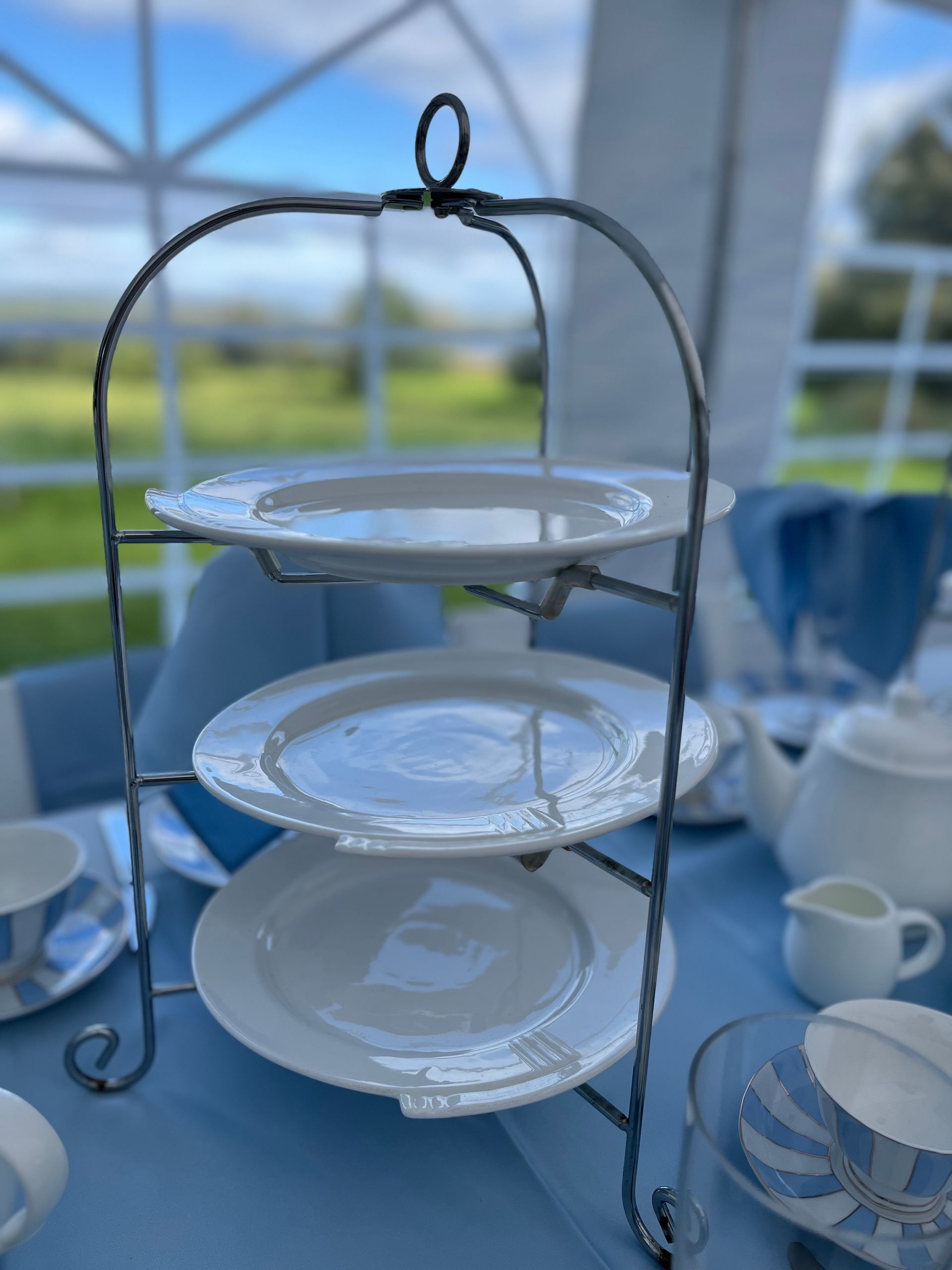 Three-tier white cake stand on a blue table at a bright outdoor table setting.