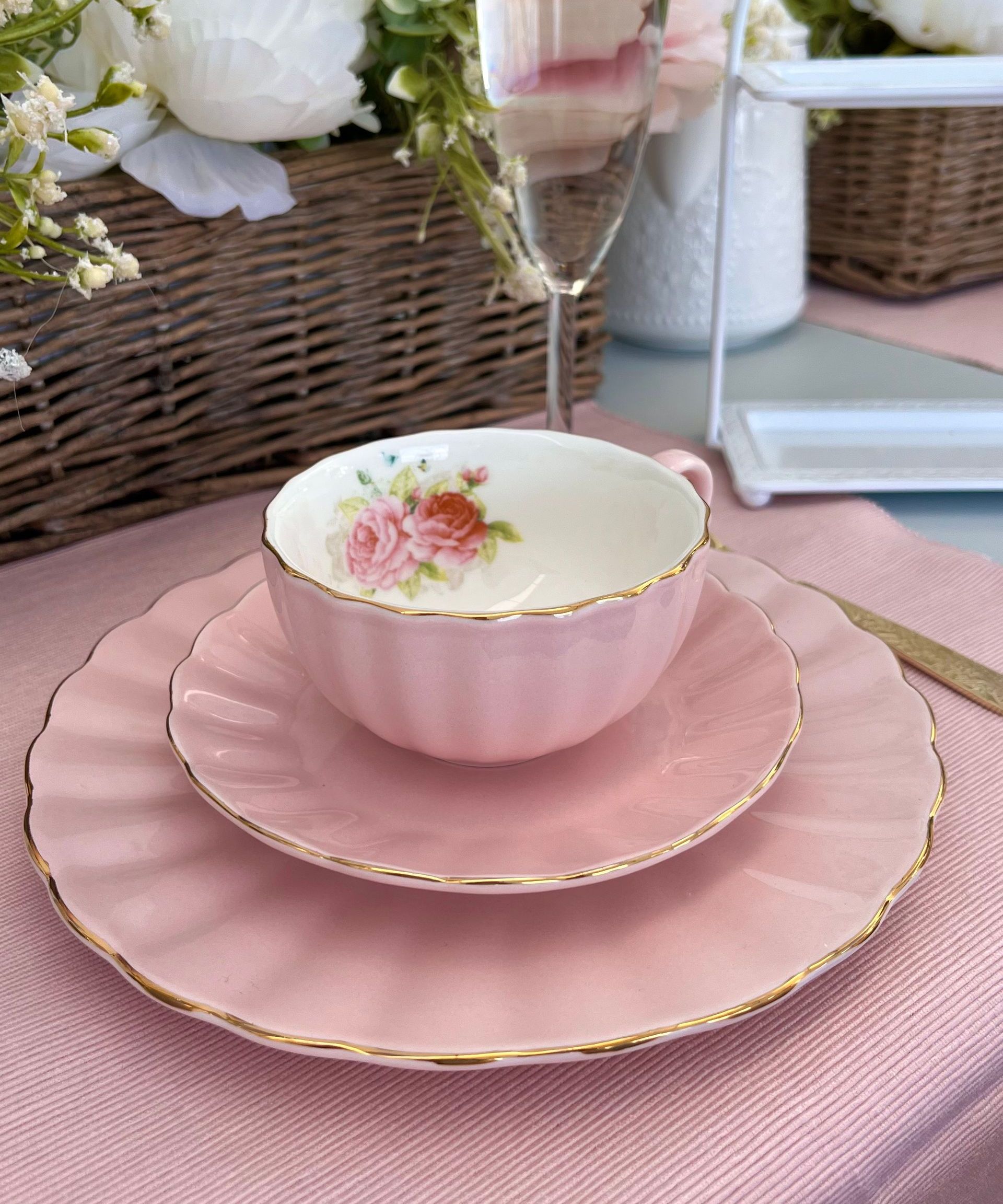 Pink teacup and saucer with gold trim on a matching pink plate, set on a pink tablecloth