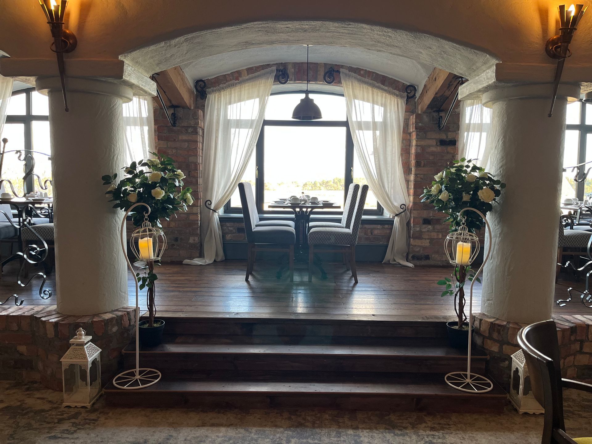 Elegant foyer with arched windows, draped curtains, a table, and floral arrangements on either side of steps