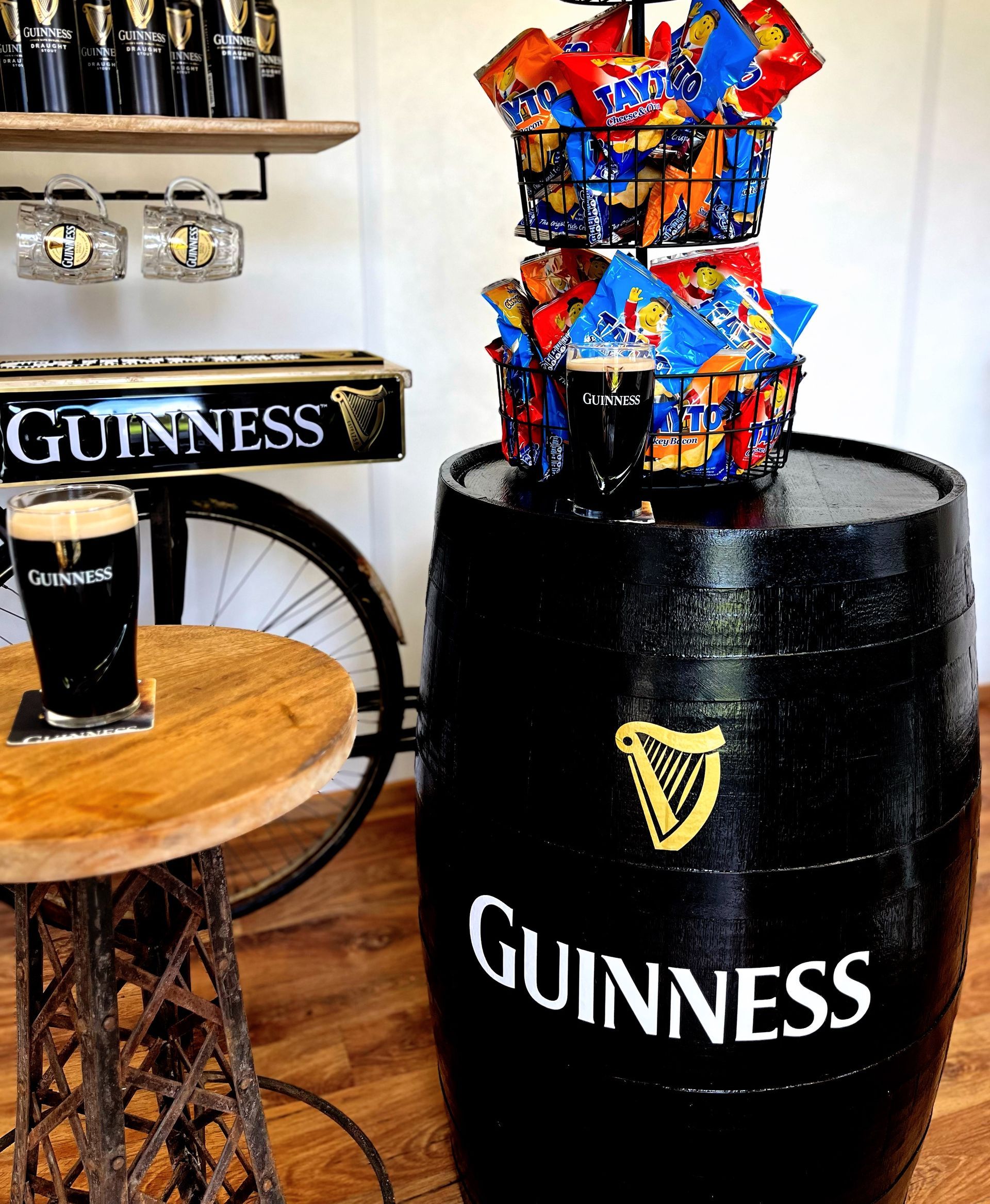 Guinness display with a black barrel, pint glass, and colorful snack tower on a wooden floor
