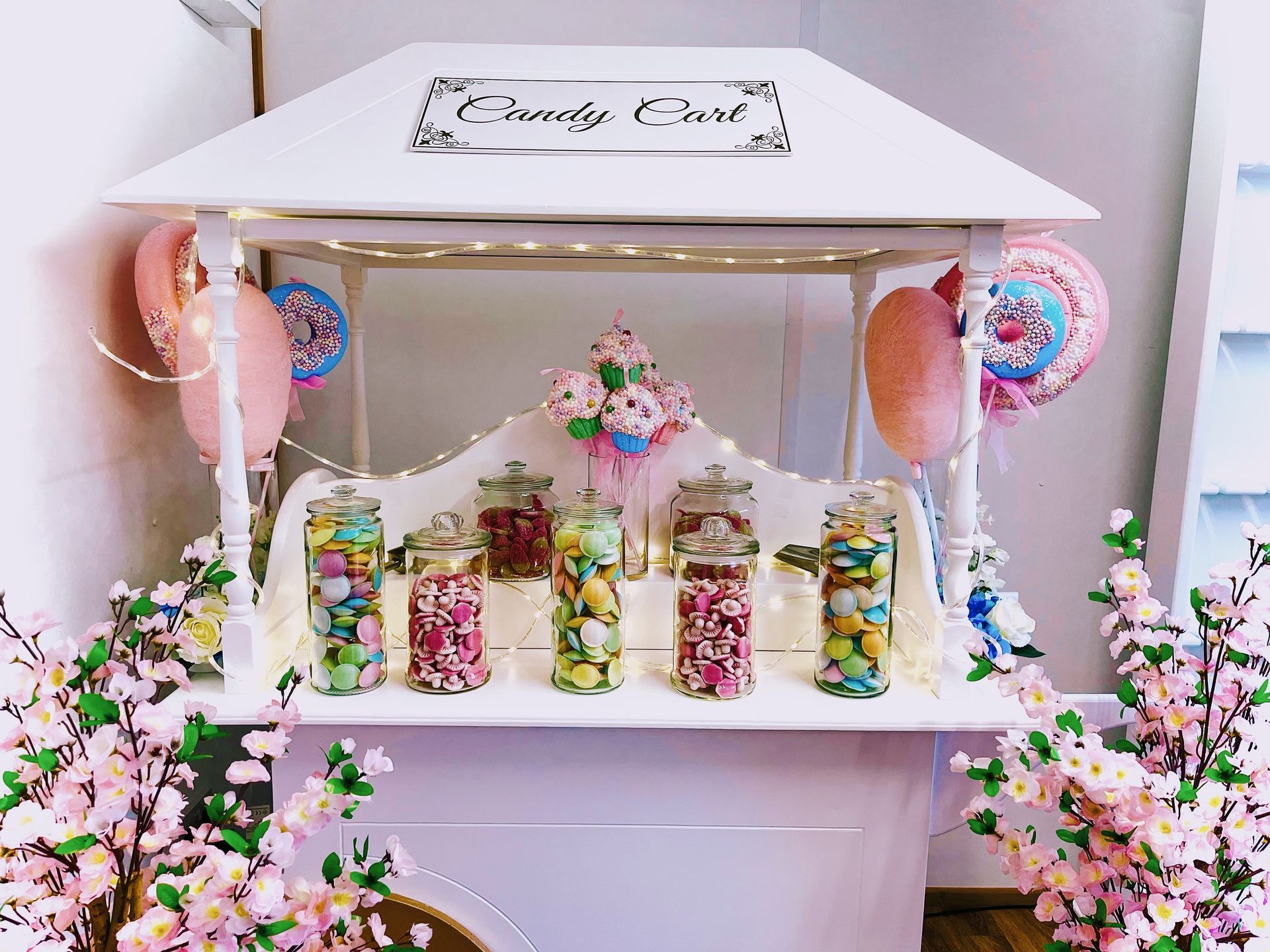 Pink candy cart with jars, pastel flowers, and balloons for a festive dessert display