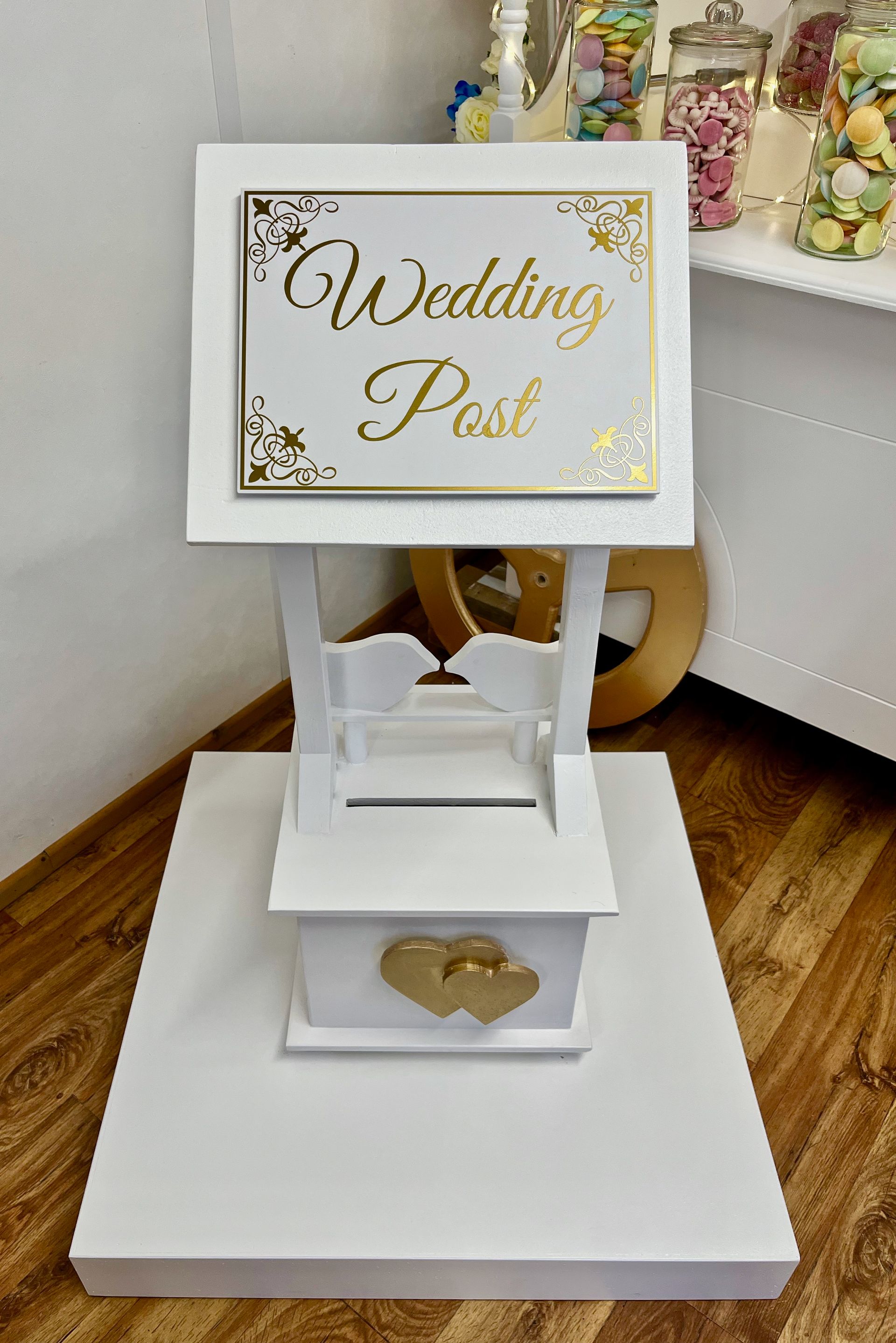 White wedding post box with gold lettering and floral accents on a white base indoors
