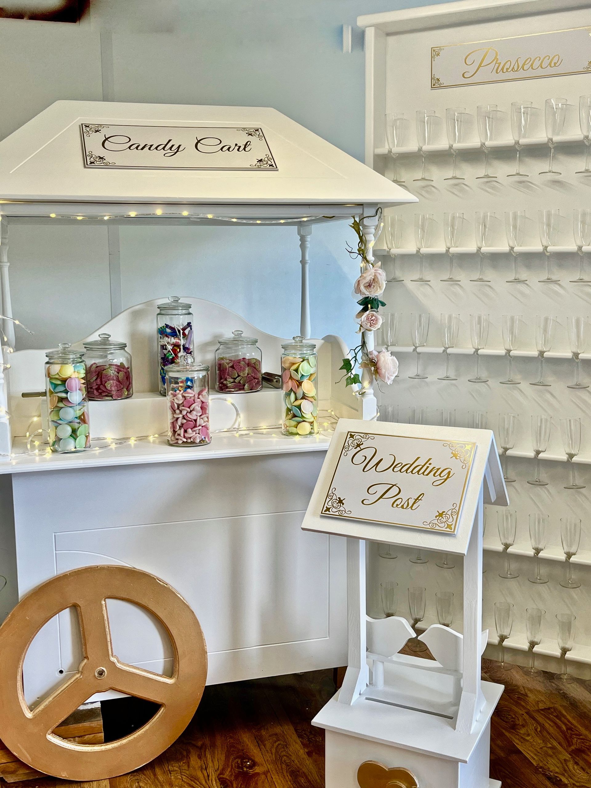 White drink cart with cups, bottles, and floral signs beside a gold peace sign decoration