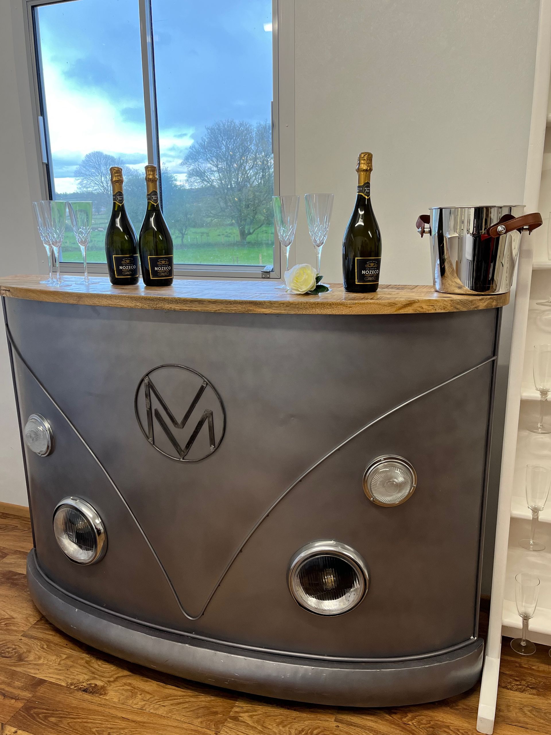 Silver curved bar with bottle display, champagne glasses, and a large window behind it