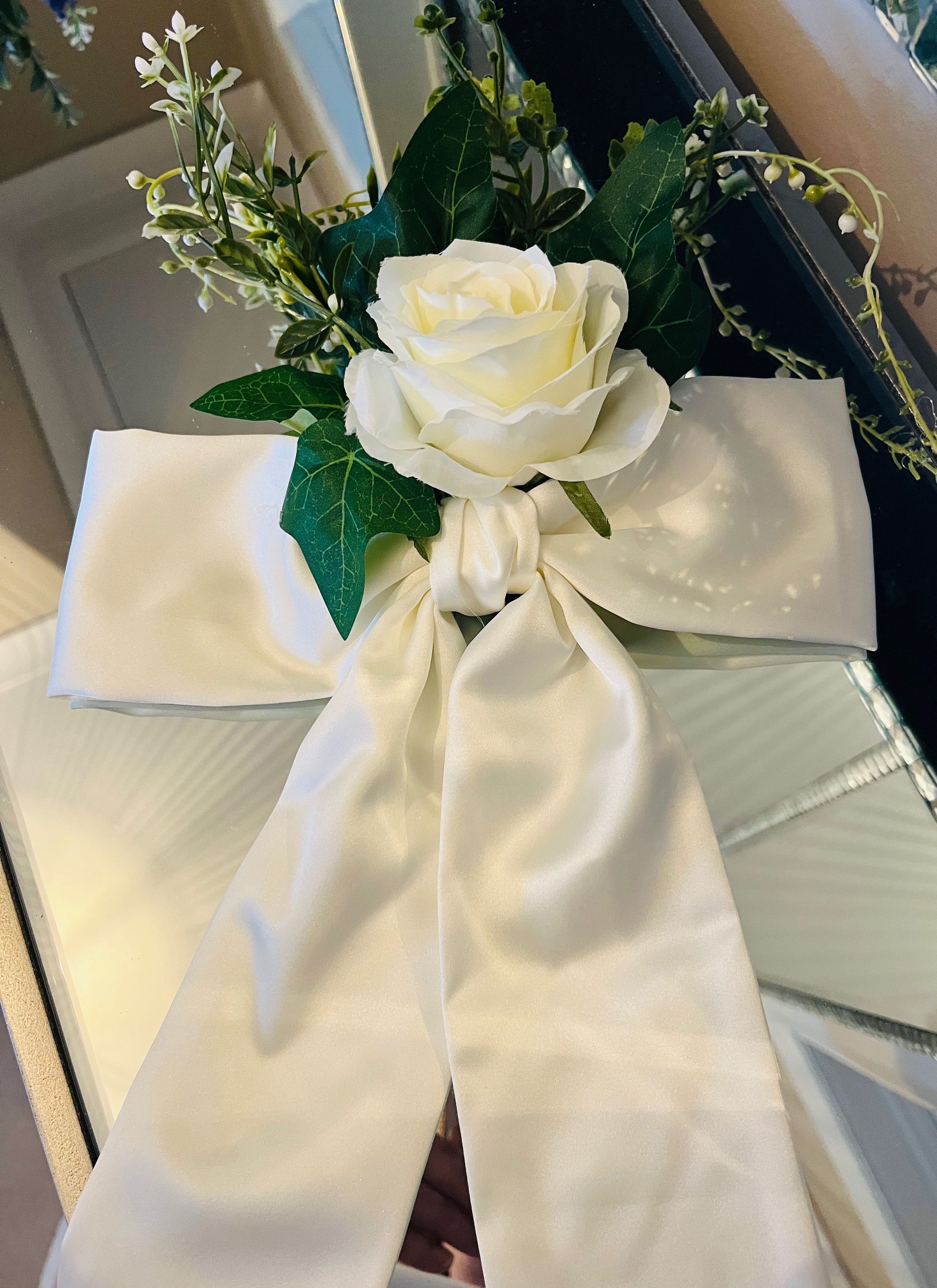 White satin bow with a rose centerpiece and greenery on a chair back