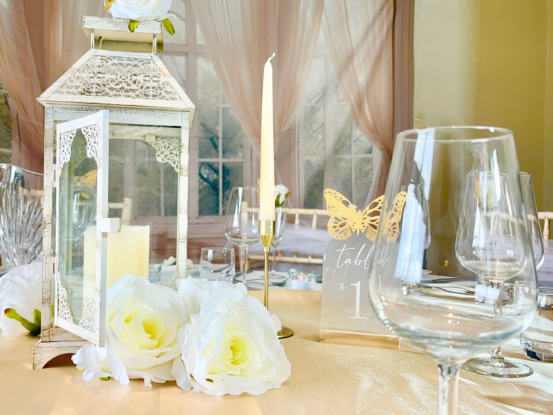 Decorated wedding table with white lantern, flowers, candles, and glassware in soft beige drapery