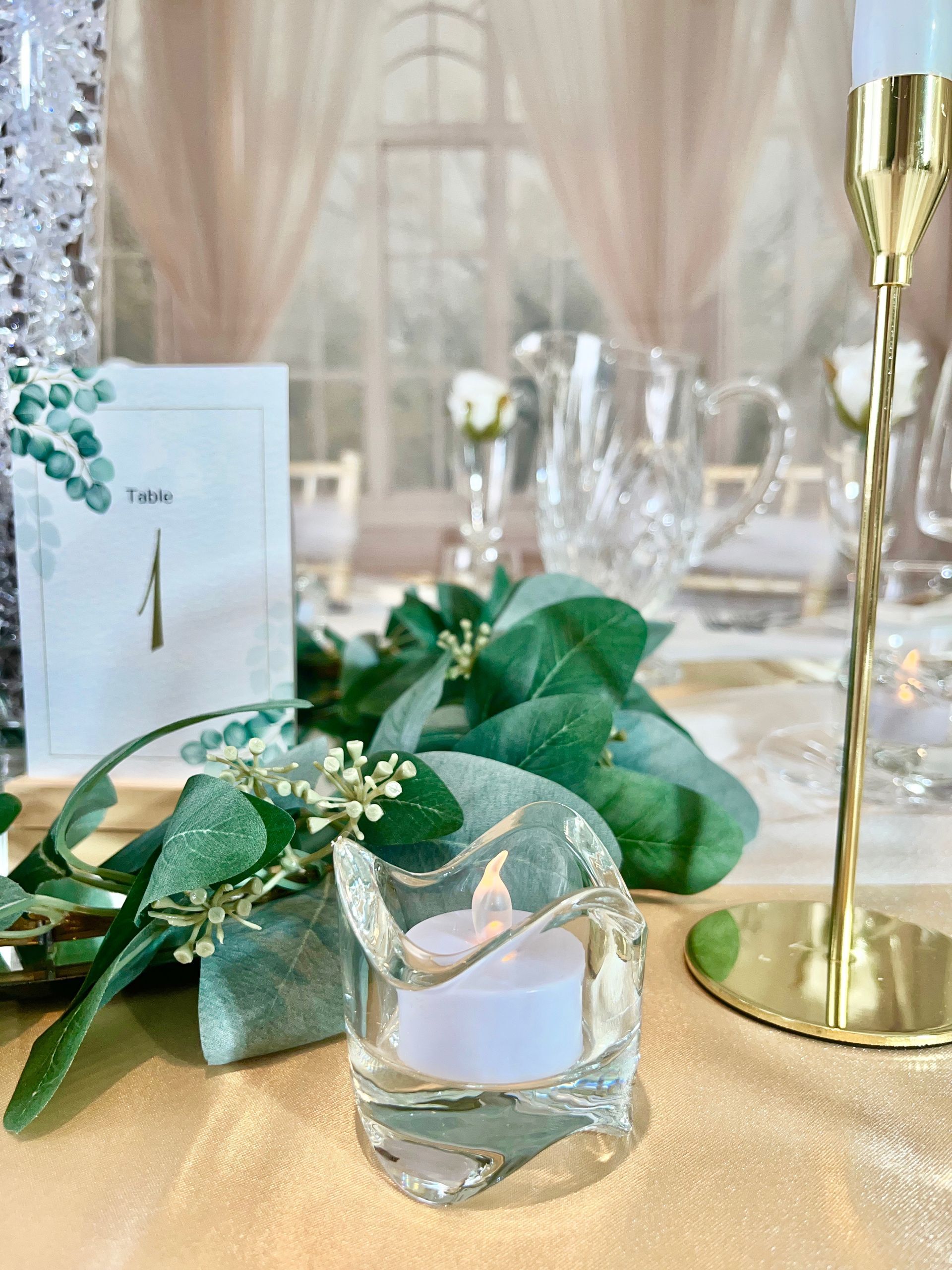 Elegant gold-and-green table setting with candle, floral decor, and champagne flute on a lace tablecloth